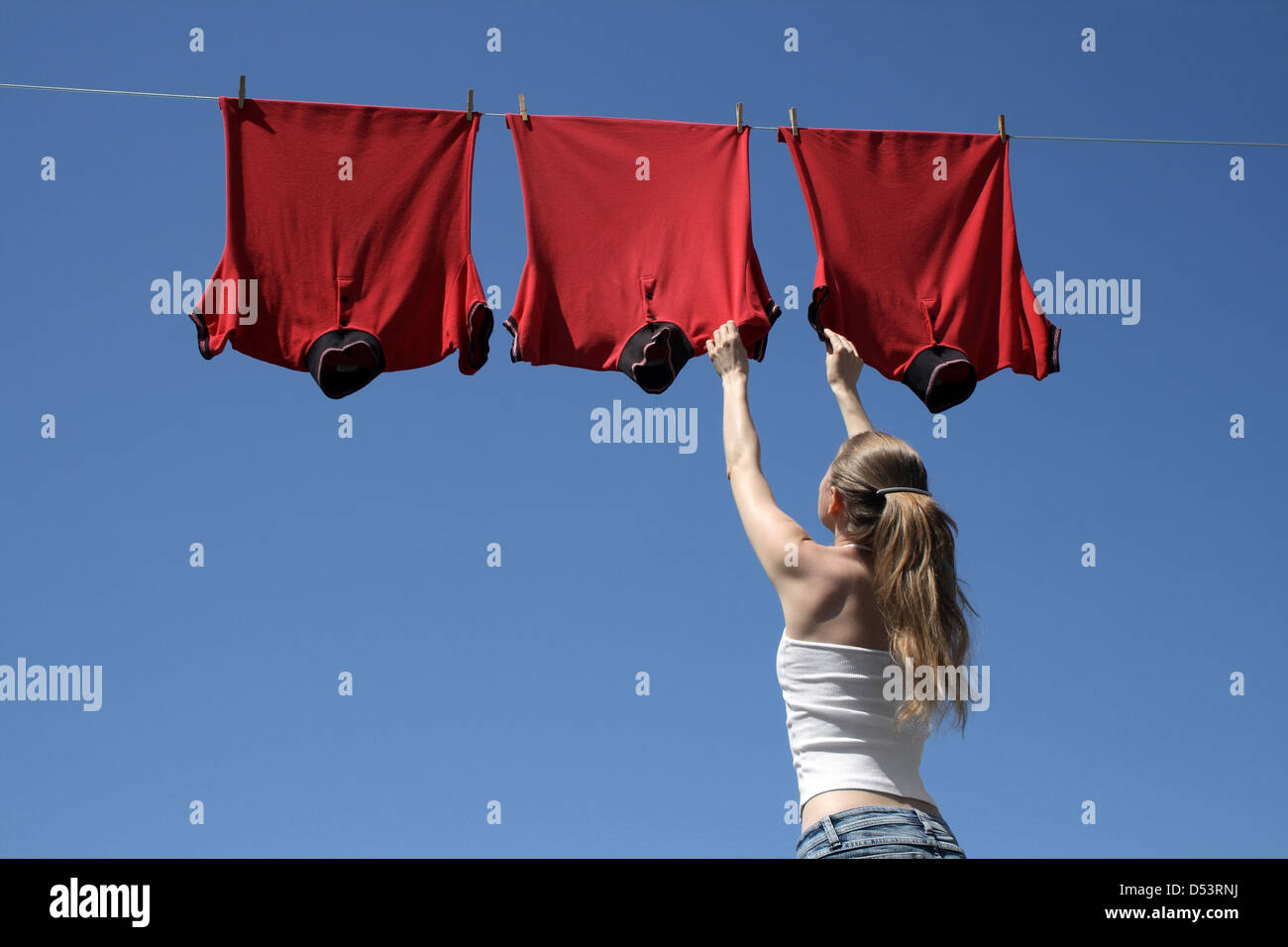 Jeune femme d'atteindre l'entreprise rouge t-shirts qui suspendre pour sécher dans une brise d'été sur une ligne de vêtements. Banque D'Images