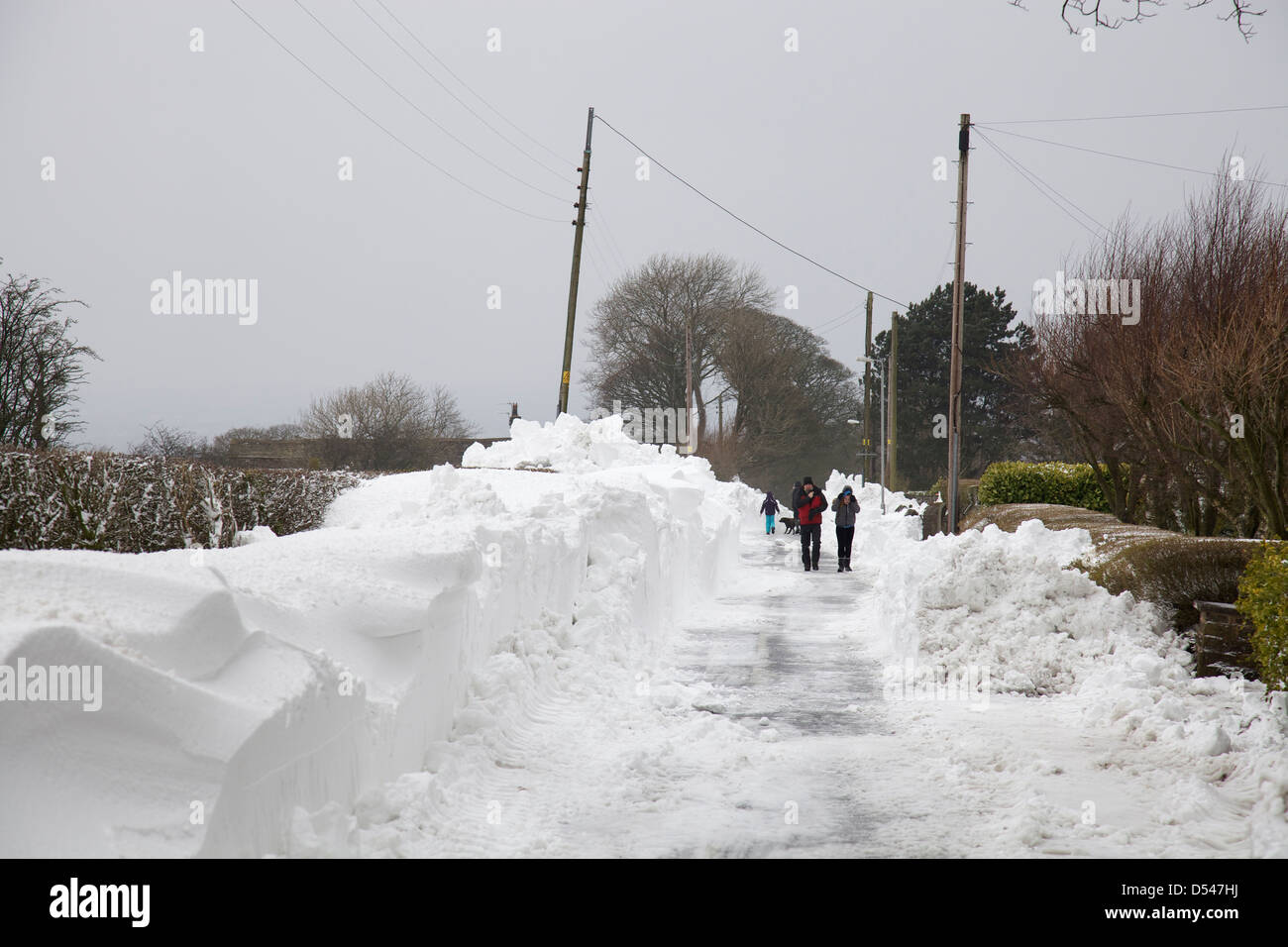 Les gens qui marchent à côté des amoncellements de neige sur un chemin déblayé récemment dans le Lancashire Banque D'Images