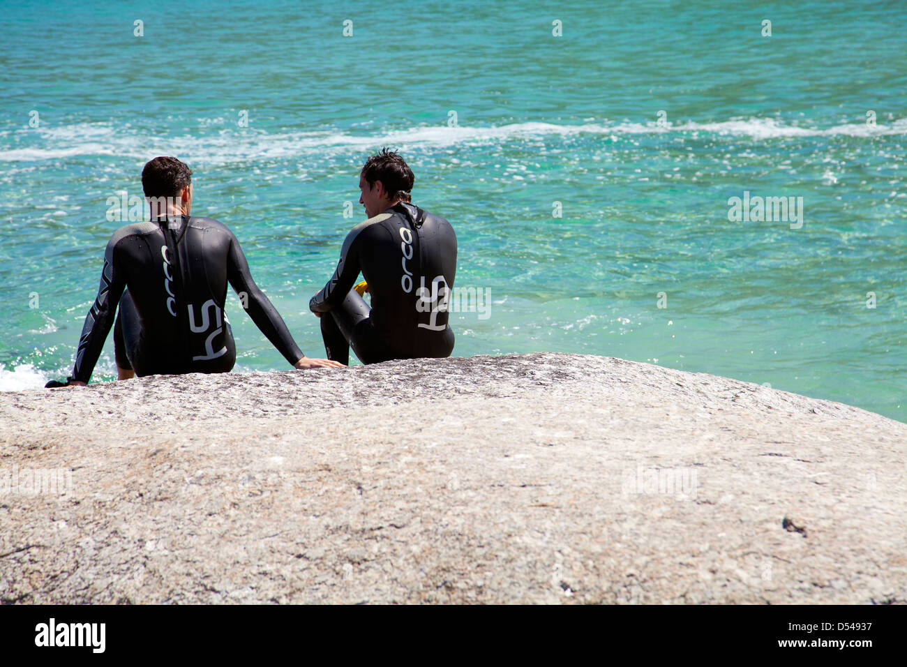 Deux nageurs en combinaisons s'asseoir sur Rock prendre du repos à la plage de Camps Bay - Cape Town, Afrique du Sud Banque D'Images