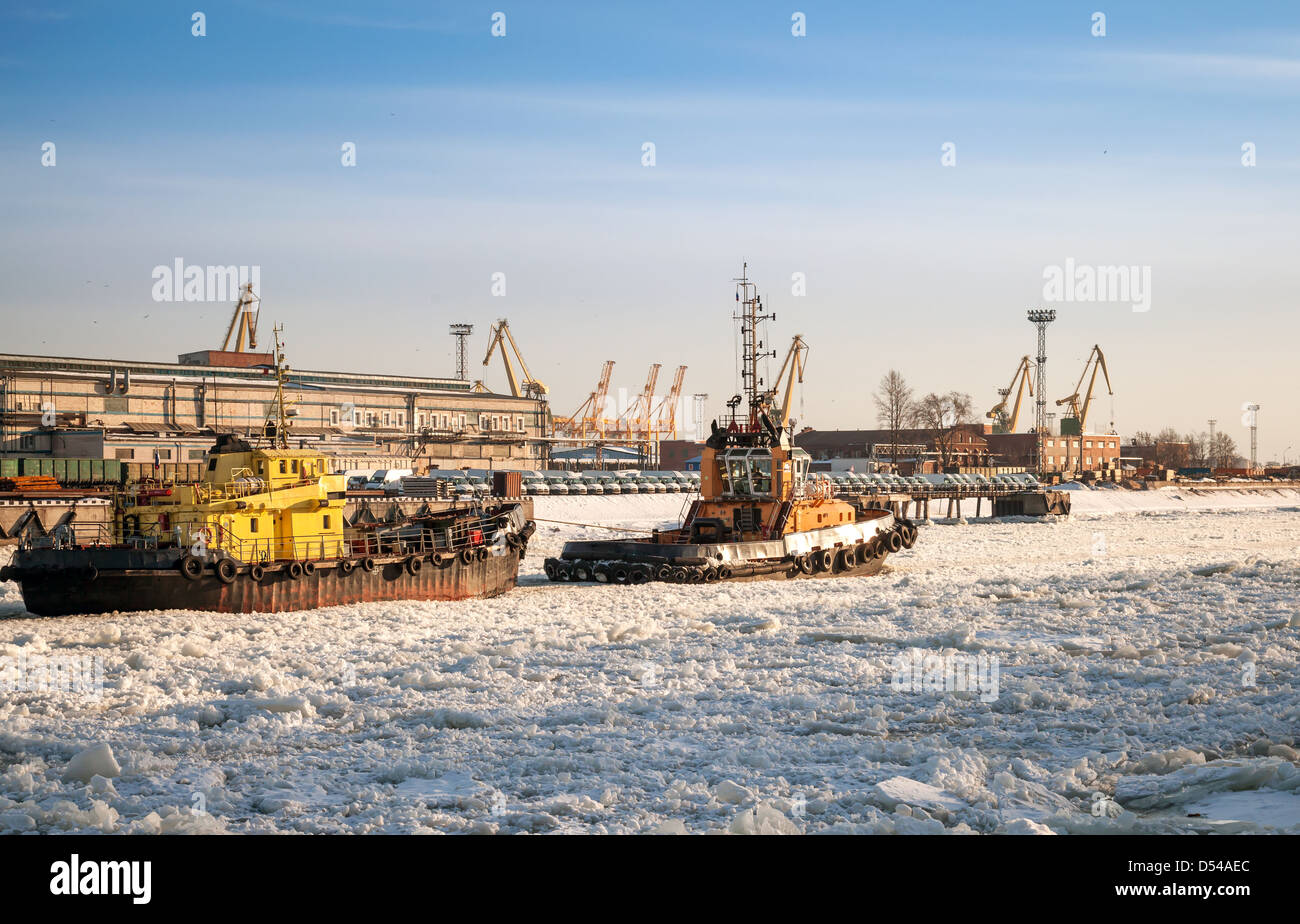 Petit bateau remorqueur va avec navire à travers le canal de glace dans le port de Saint-Pétersbourg port marchand Banque D'Images