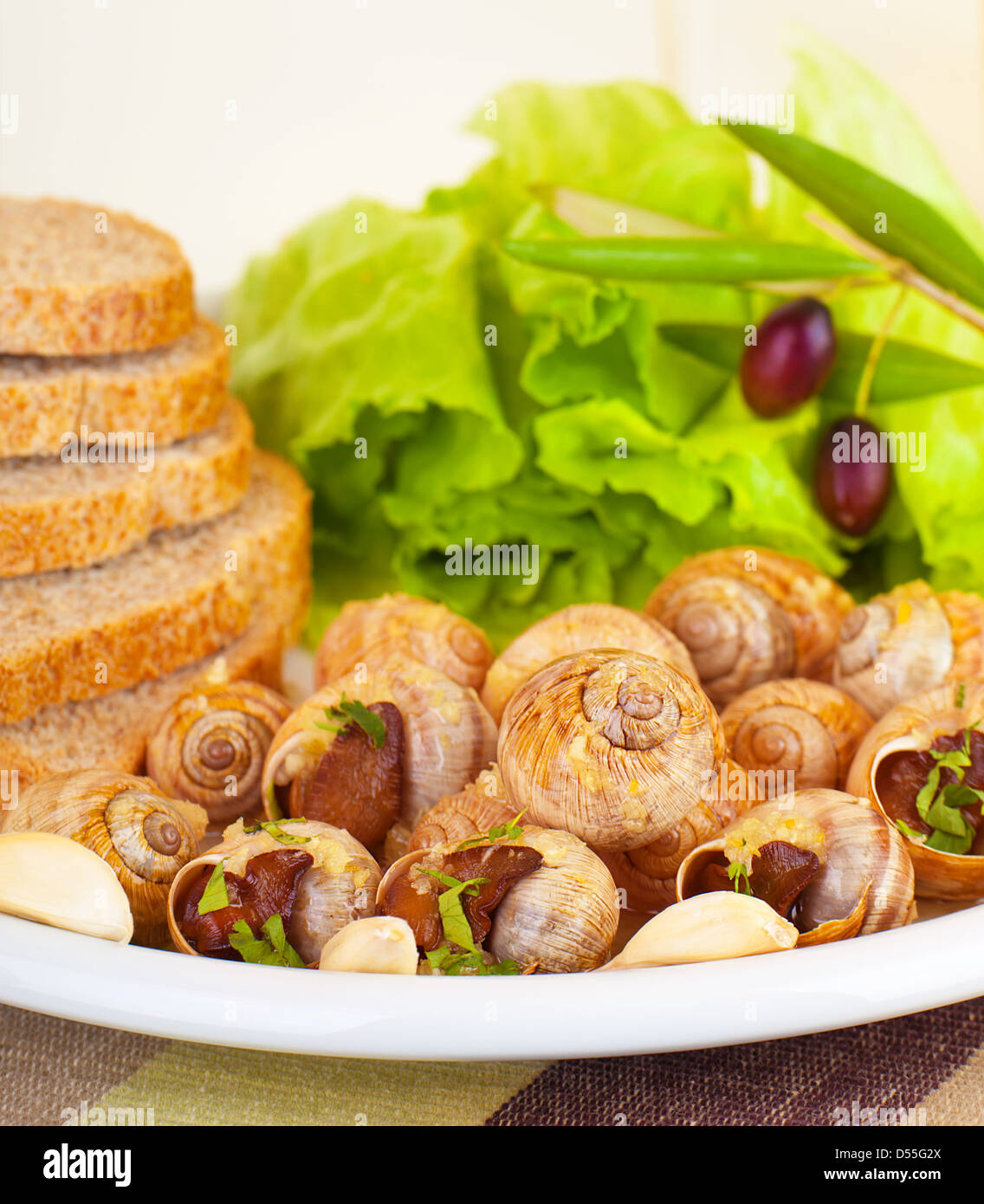 L'escargot préparé savoureux avec des produits frais salade de laitue verte, olives noires, du pain et de l'ail sur plaque blanche en restaurant, repas de luxe Banque D'Images