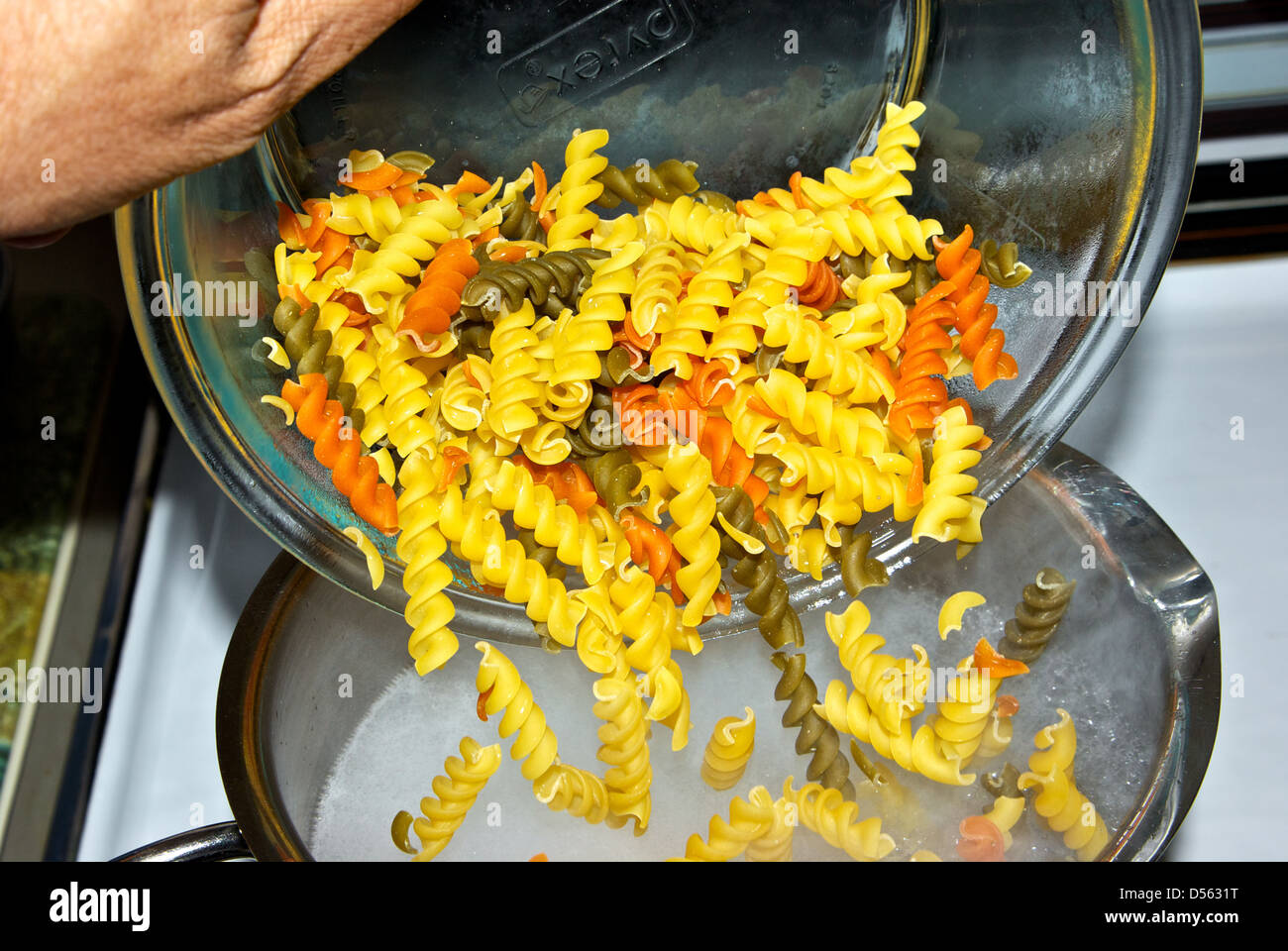 Bol Verser les pâtes rotini tricolore non cuites à sec dans l'eau bouillante rapidement pot Banque D'Images