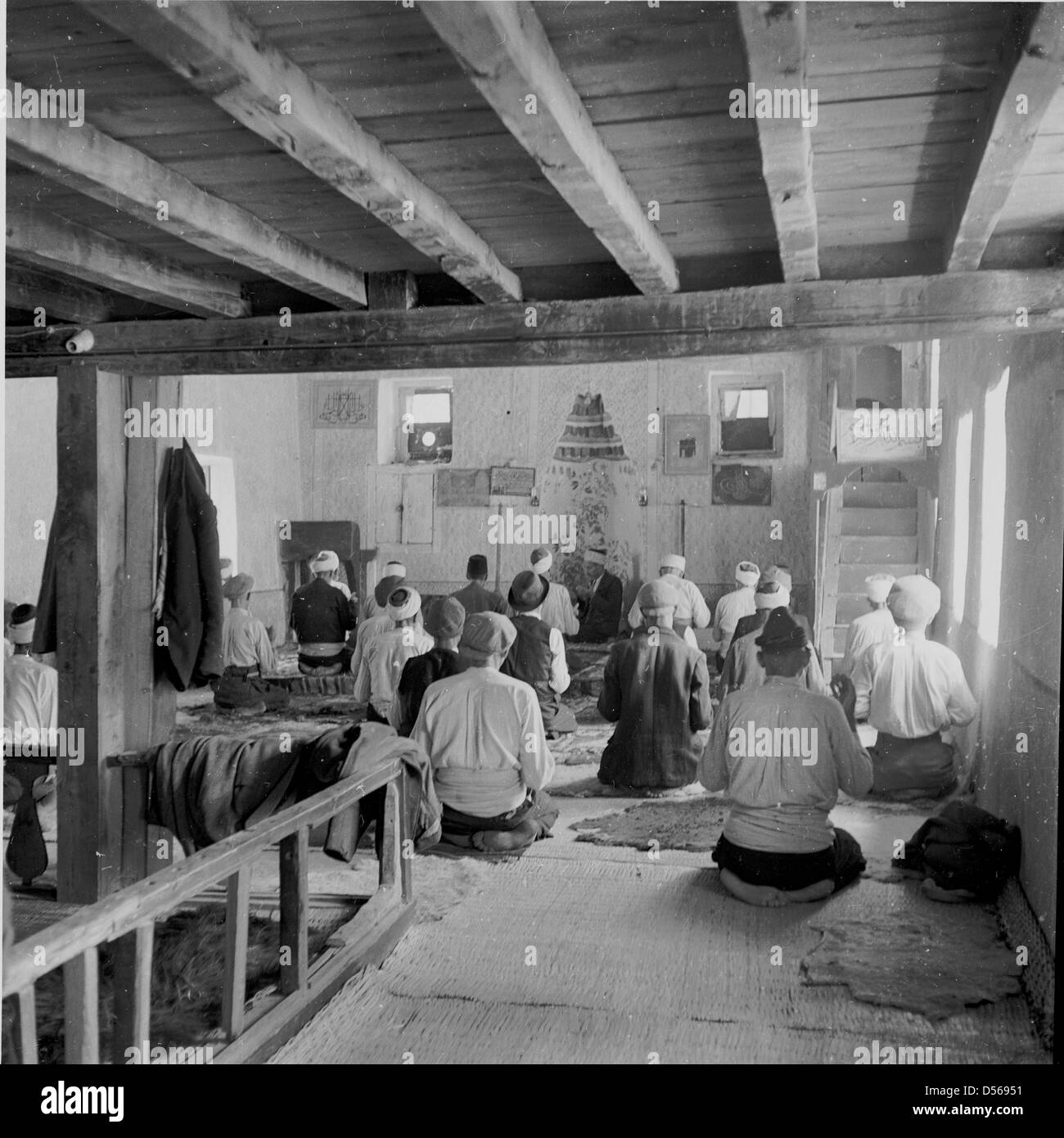 1950 historique. La Bulgarie. Réunion de prière musulmane. Les hommes assis sur les tapis à l'intérieur d'une vieille grange en prière. Banque D'Images
