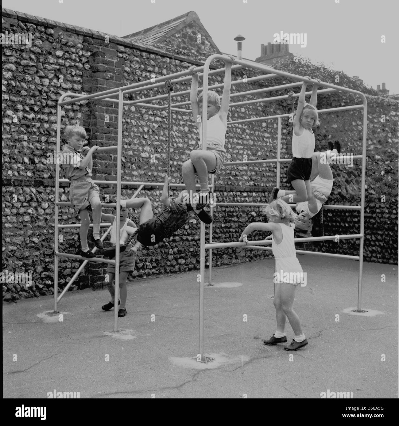 Historique, 1950. L'Angleterre. Les jeunes enfants jouer dehors en aire de jeux sur un métal d'escalade au cours d'une école maternelle PE session. Banque D'Images