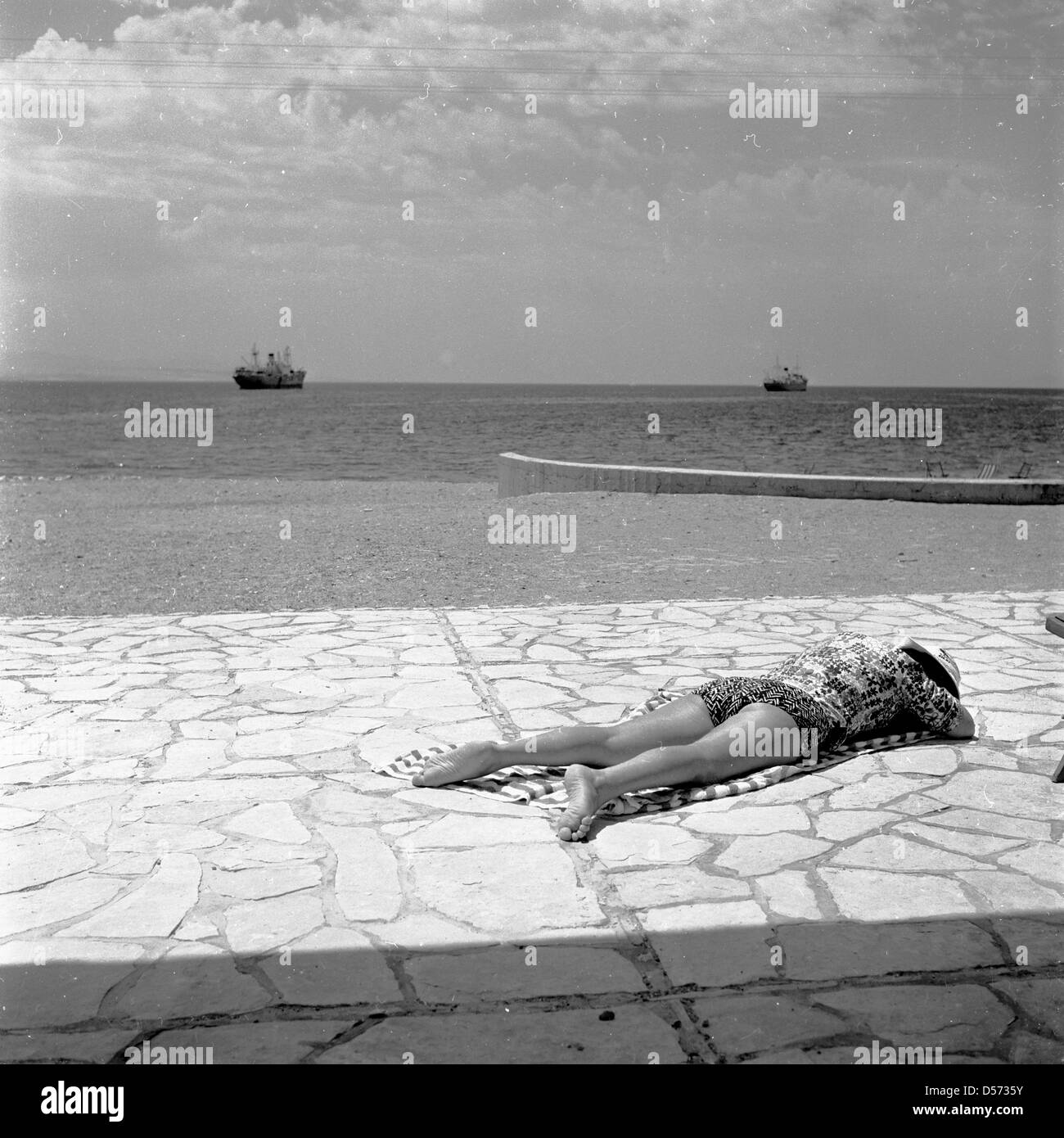 1950 historique. Israël. Dame se trouve sur une serviette sur un mur à carreaux de soleil. Banque D'Images