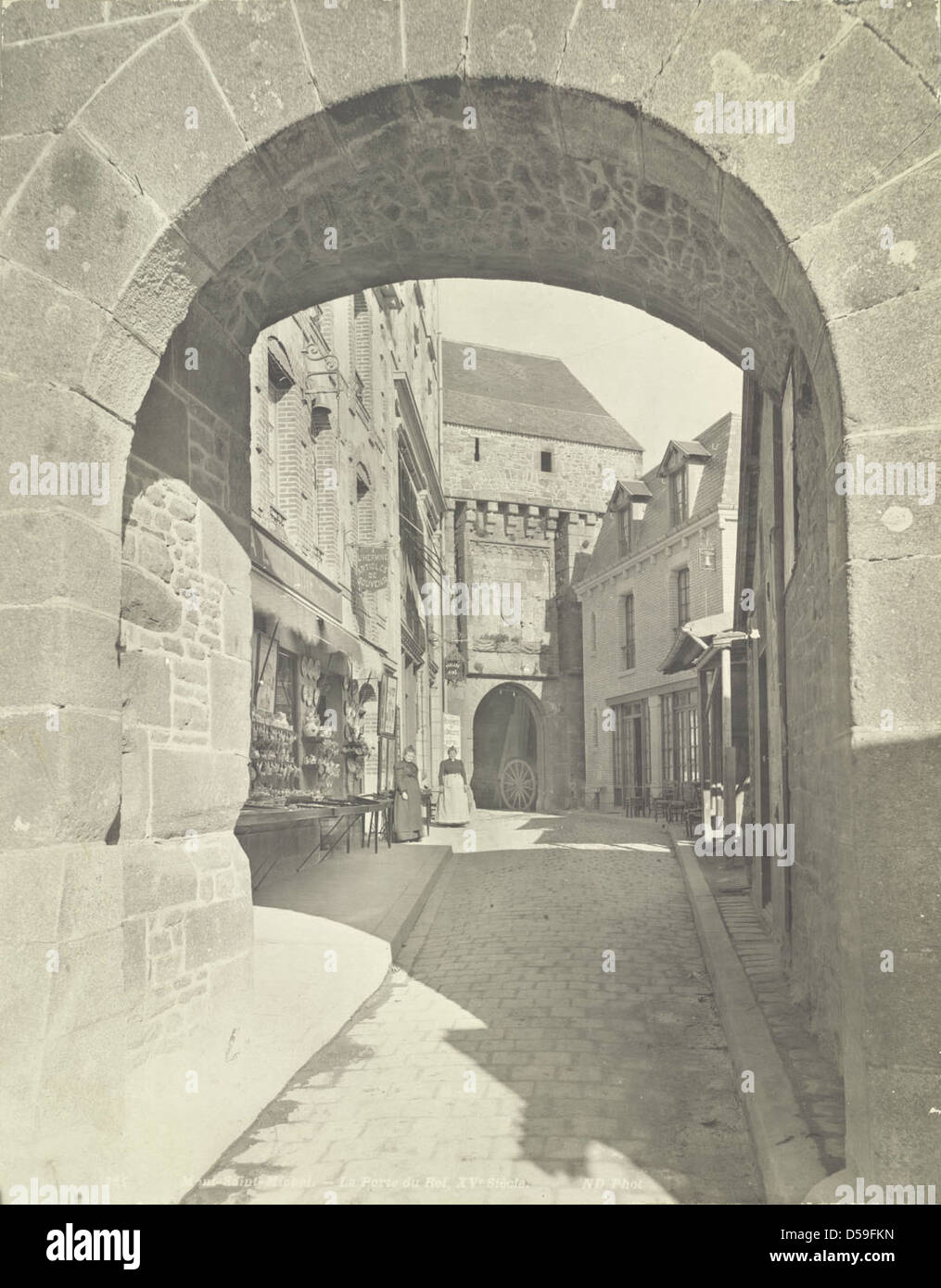 La porte du Roi au Mont Saint-Michel en France, avec des portails voûtés et des trottoirs pavés. Les détails architecturaux de la porte comprennent le corbeling et le paysage urbain historique de l'île. Banque D'Images