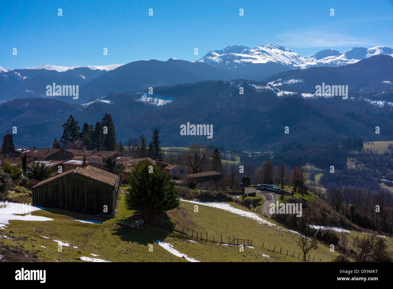 Vue vers les Pyrénées enneigés au-dessus de forêts sombres, avec petit village, ciel bleu Banque D'Images