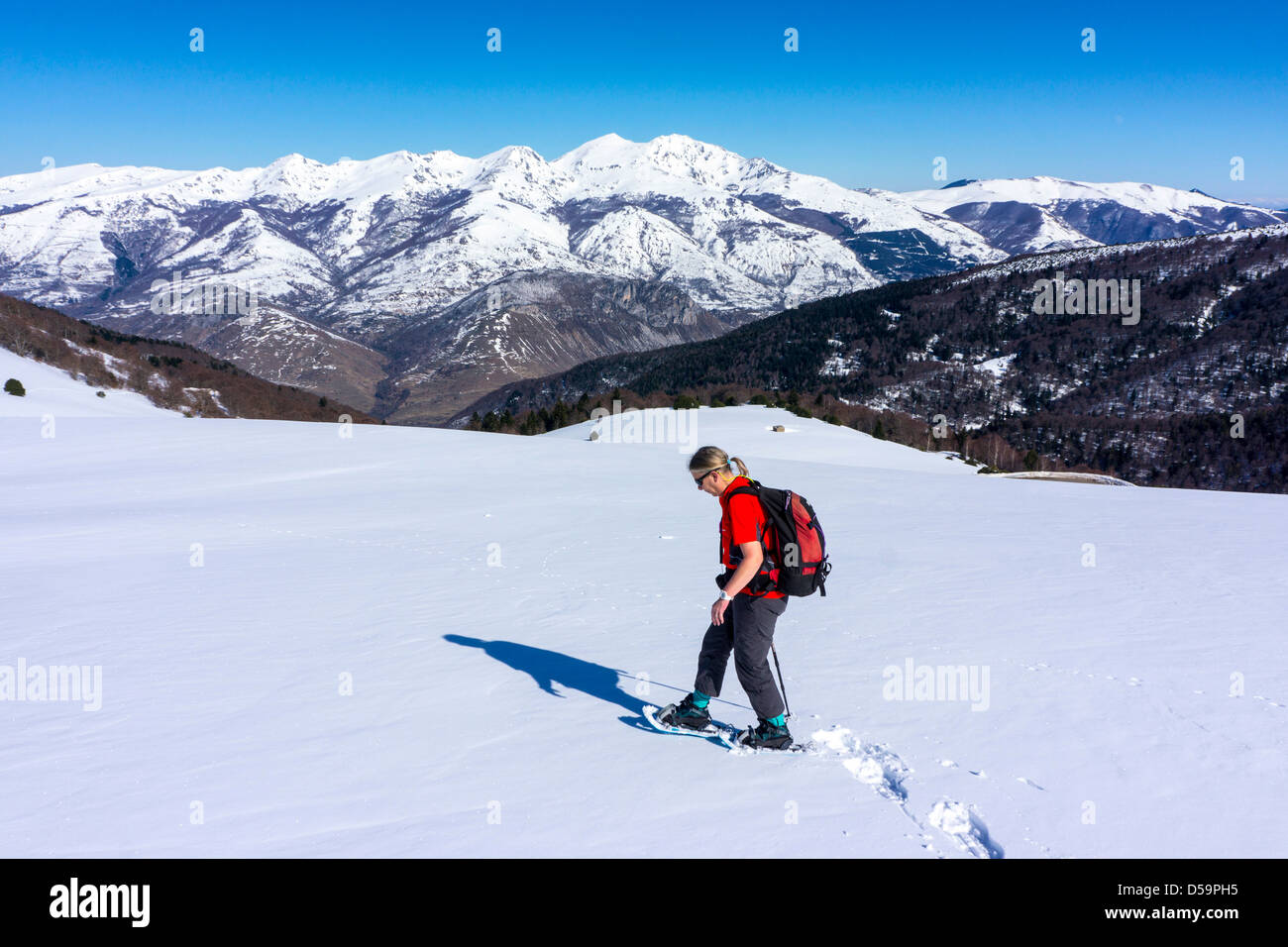 Femme en rouge avec des raquettes sur pente de neige, Plateau de Beille, Pyrénées françaises Banque D'Images