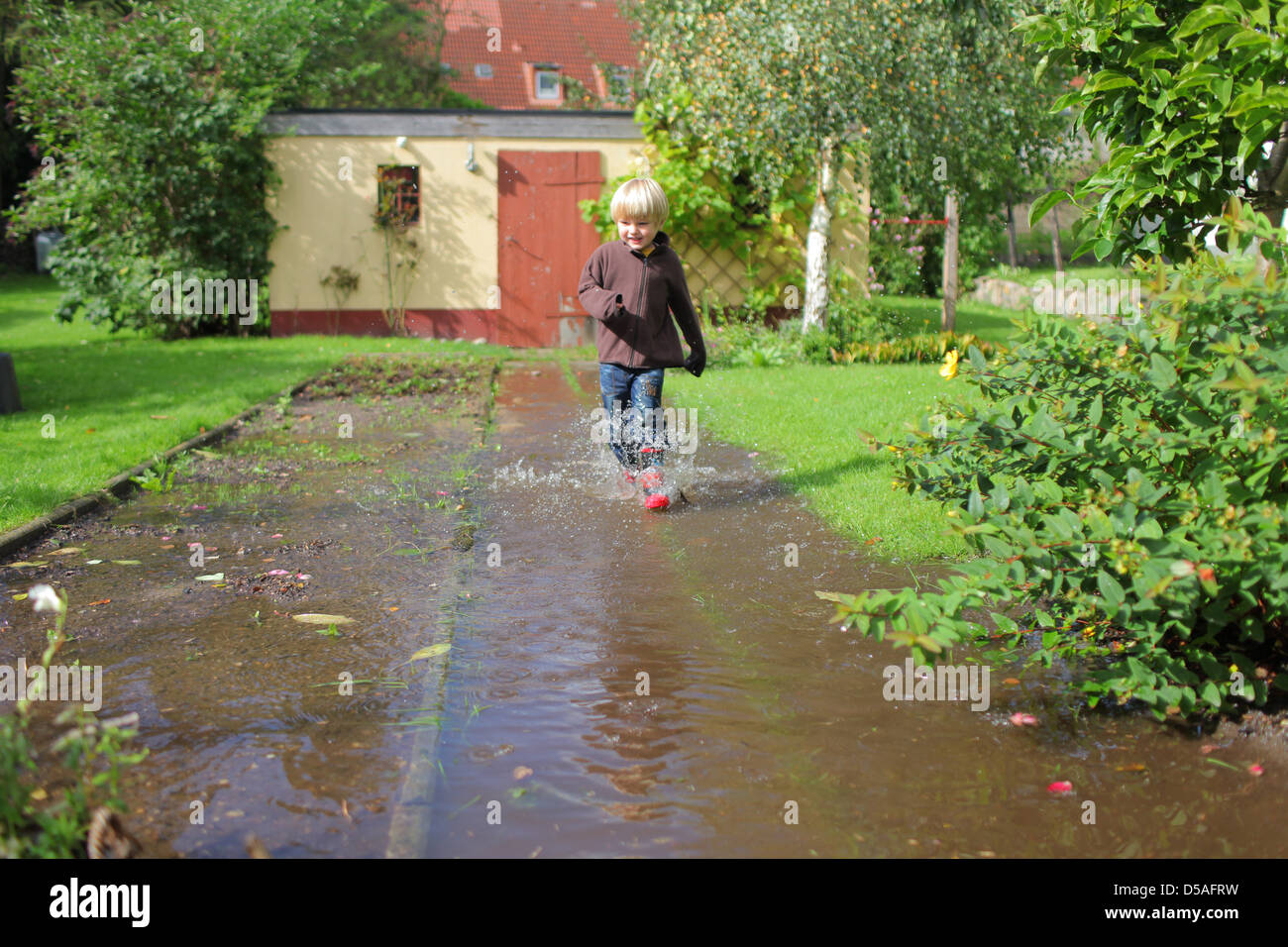 Handewitt, Allemagne, un garçon s'exécute en bottes de caoutchouc à travers un jardin inondé Banque D'Images