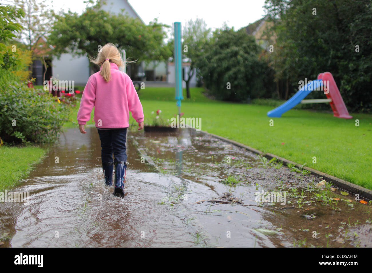 Handewitt, Allemagne, une fille court en bottes de caoutchouc à travers un jardin inondé Banque D'Images