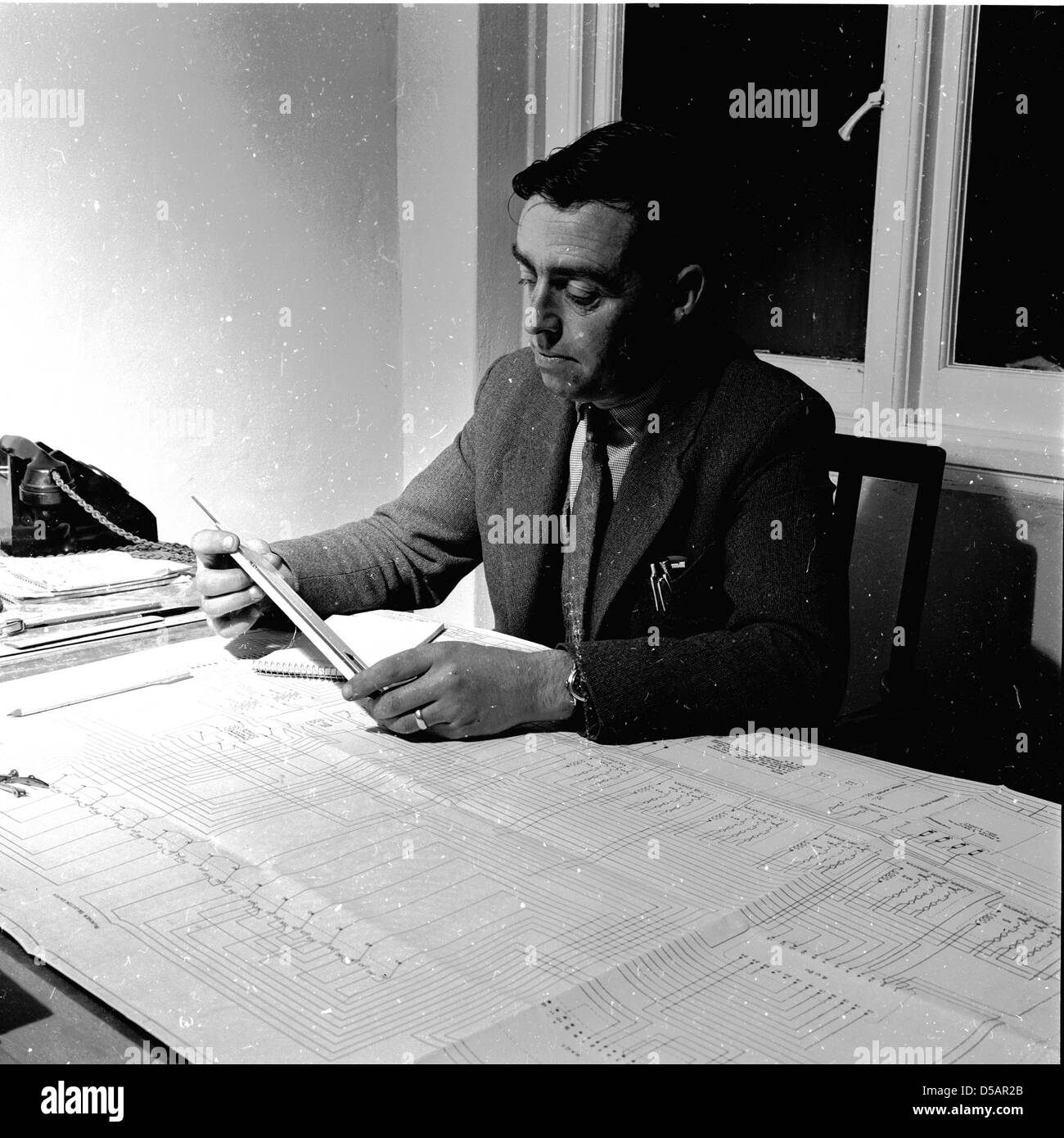 Historique, 1950. Un homme travaille à son bureau sur une grande feuille de papier avec des graphiques. Banque D'Images