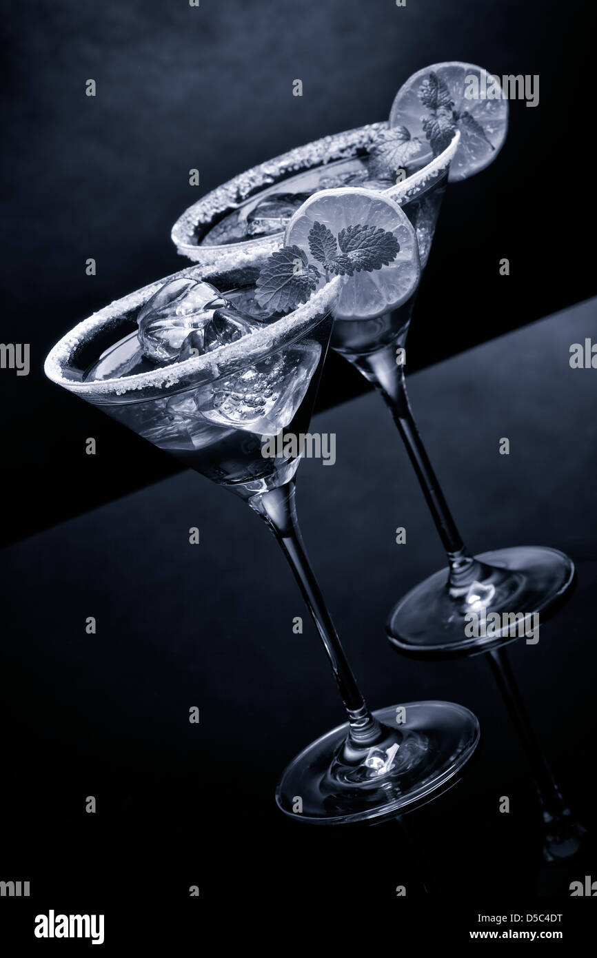 Des cocktails dans des verres à martini avec bords sucrées, lime slice, cubes de glace, feuille de menthe. Noir et blanc de l'image dans les tons bleus. Banque D'Images