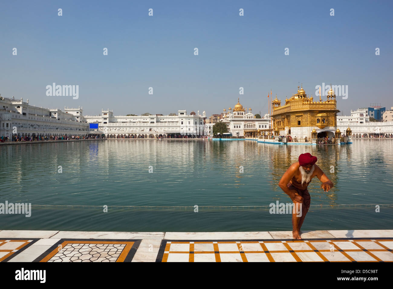 Un dévot Sikh faisant un pas hors de la piscine Sainte à l'intérieur du complexe du temple d'or d'Amritsar Punjab Inde sous un ciel bleu Banque D'Images
