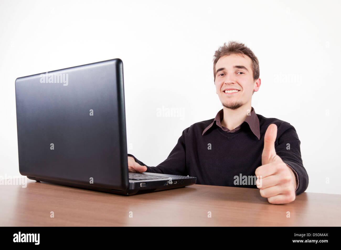 Young man holding up avec un ordinateur portable sur un bureau Banque D'Images