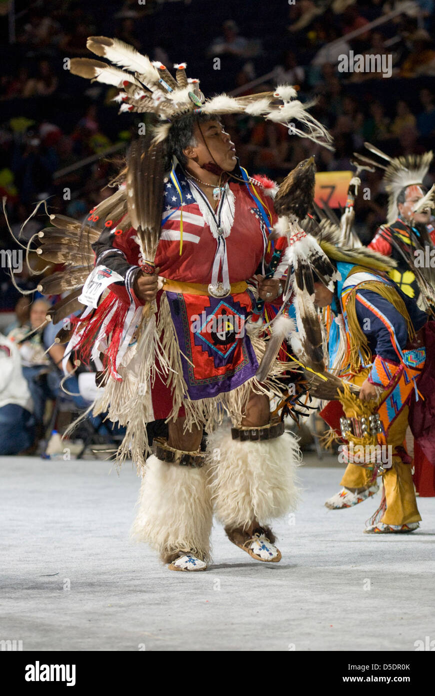Une cérémonie de Powwow de 2007 mettant en vedette un participant tenant le drapeau américain tout en étant vêtu de regalia amérindiens traditionnels. Les costumes vibrants, la peinture du visage et les coiffes à plumes colorées soulignent l'importance culturelle de cette danse rituelle. Banque D'Images
