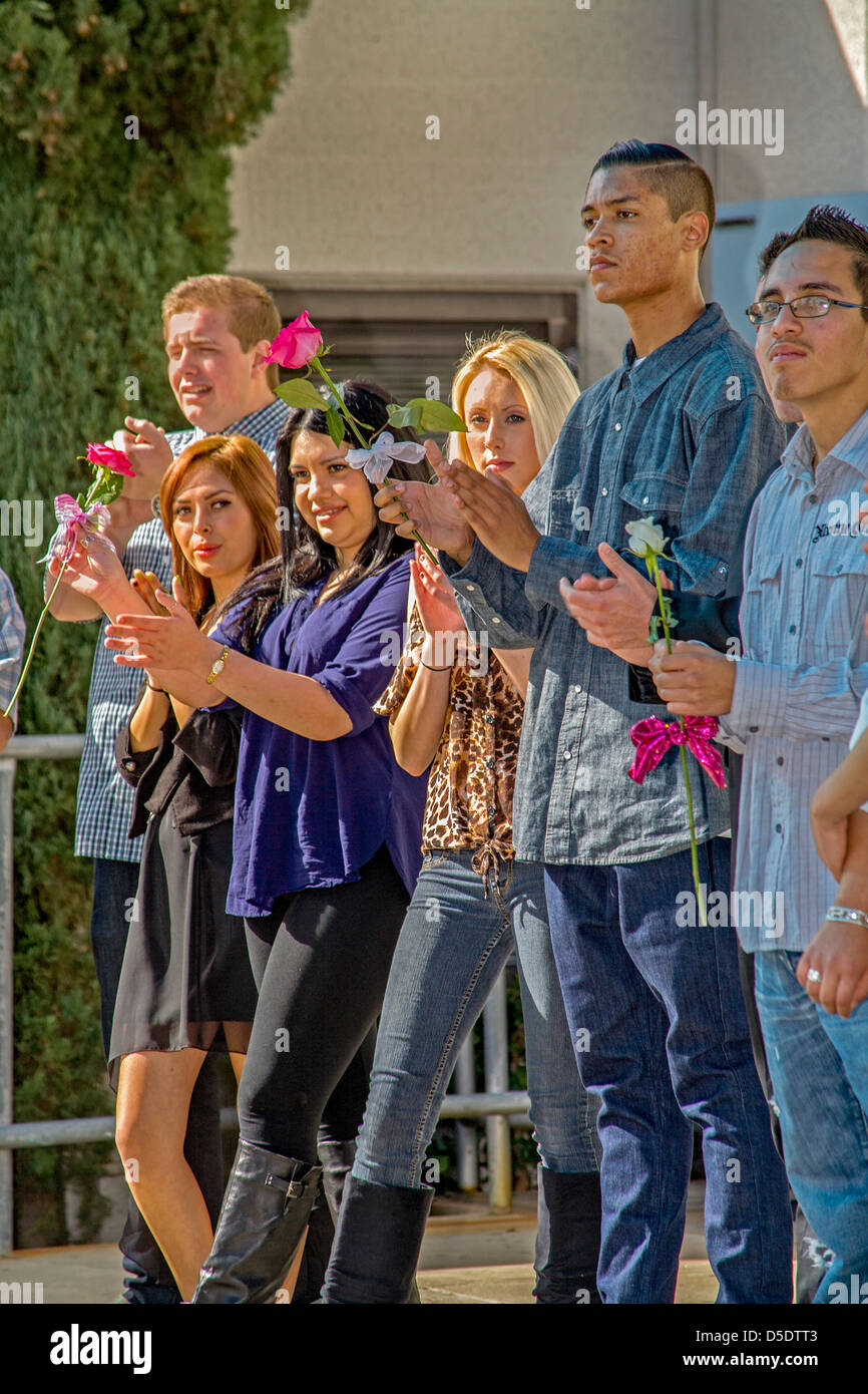 Holding roses comme graduation gifts, habillé décontracté cheer camarades étudiants le jour de la remise des diplômes à l'école secondaire de continuation. Banque D'Images