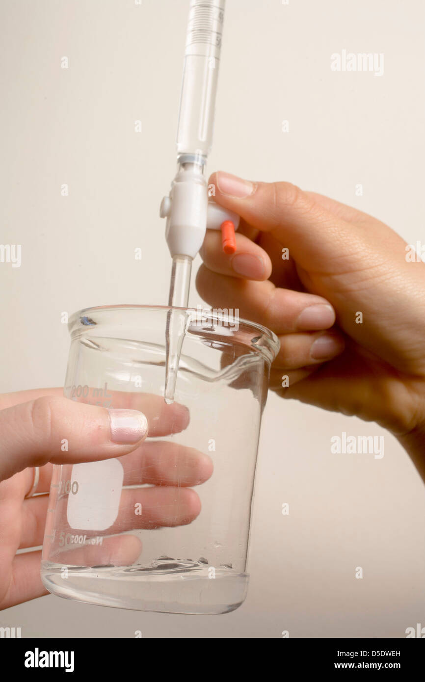 Une pipette les gouttes de vinaigre ordinaire (acide) dans un récipient contenant un volume précis d'hydroxyde de sodium (base) pour montrer le titrage Banque D'Images