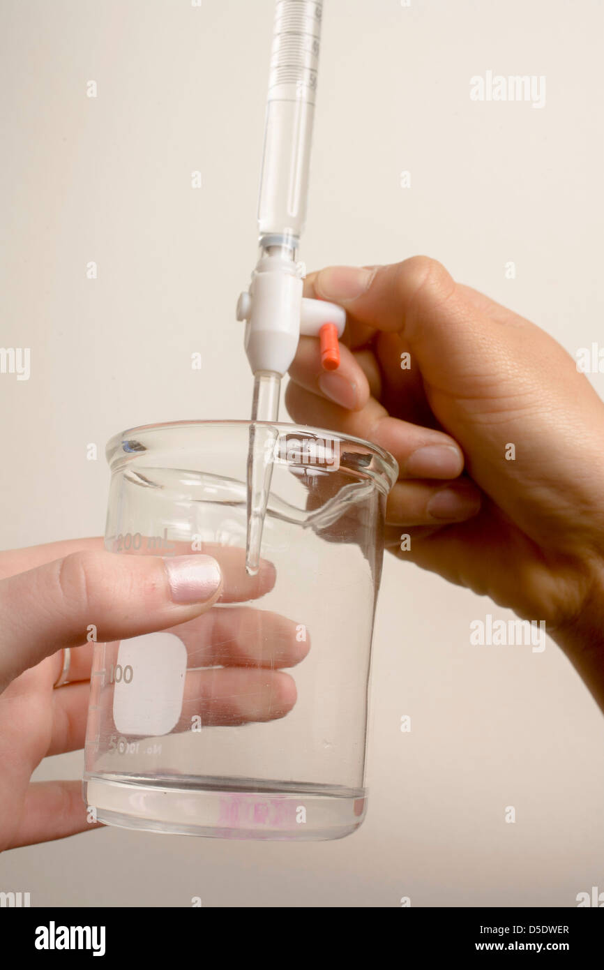 Une pipette les gouttes de vinaigre ordinaire (acide) dans un récipient contenant un volume précis d'hydroxyde de sodium (base) pour montrer le titrage Banque D'Images
