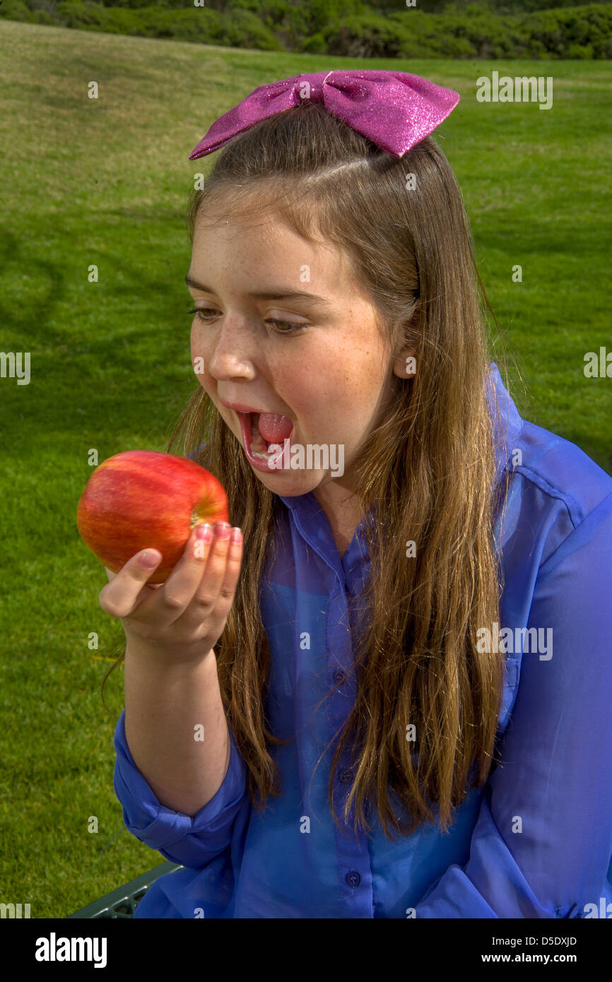 A happy young Caucasian girl mange une pomme Gala à l'extérieur dans un Lagnua Beach, CA, Parc. Banque D'Images