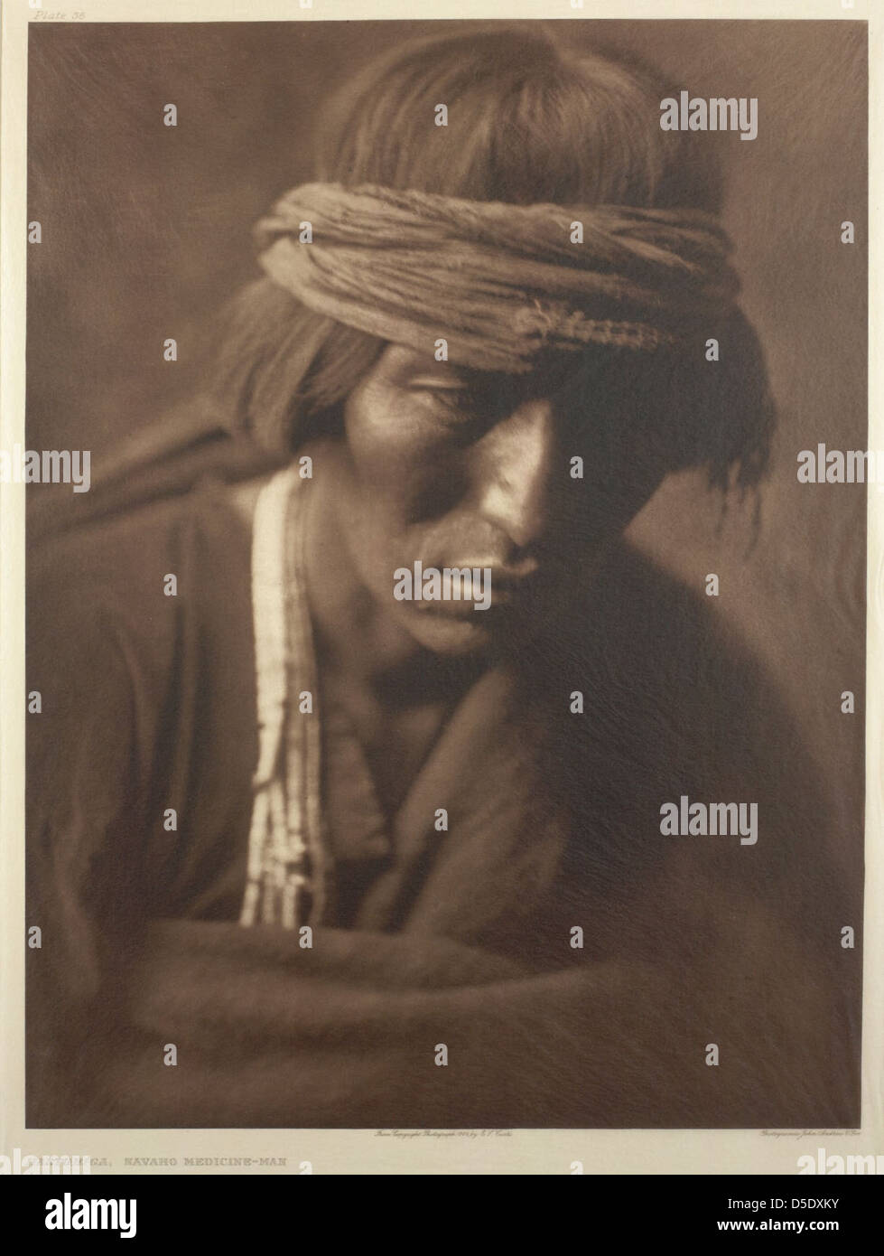 Un portrait par Edward Curtis de Hastobiga, un médecin Navaho, mettant en valeur une tenue traditionnelle, y compris un foulard. Cette image reflète le rôle culturel et spirituel des hommes de médecine au sein des tribus amérindiennes. Banque D'Images
