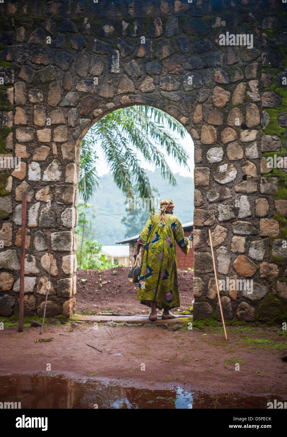 African woman walking avec canne en robe colorée d'une église en pierre archway au Cameroun Banque D'Images