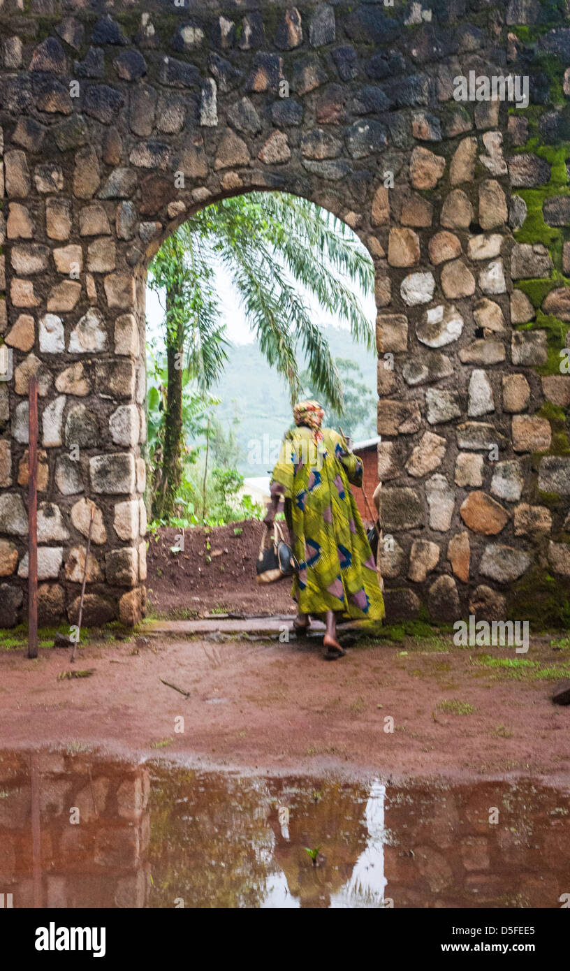 African woman walking avec canne en robe colorée d'une église en pierre archway au Cameroun Banque D'Images