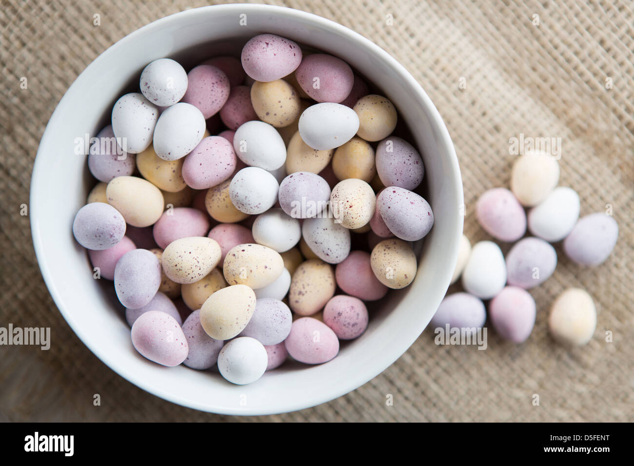 Un bol d'œufs de pâques mini à côté d'une poignée d'œufs en chocolat, placé sur un fond texturé brun Banque D'Images