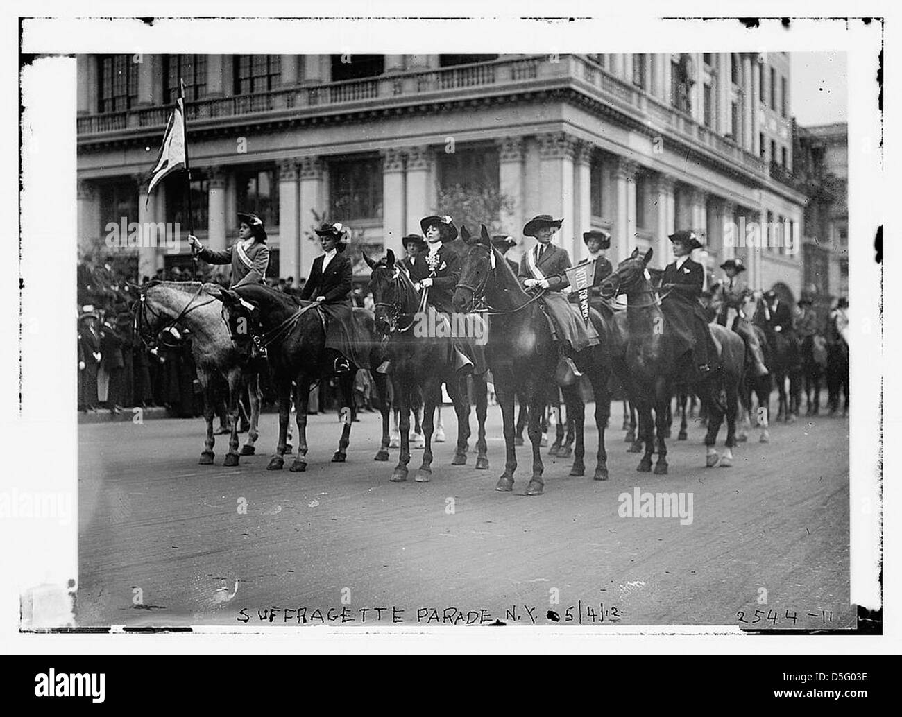 Un défilé des suffragettes des années 1910 à New York, où les femmes défilent pour le droit de vote, tenant des drapeaux et montant à cheval. Ce moment historique met en lumière le mouvement pour le suffrage féminin aux États-Unis. Banque D'Images