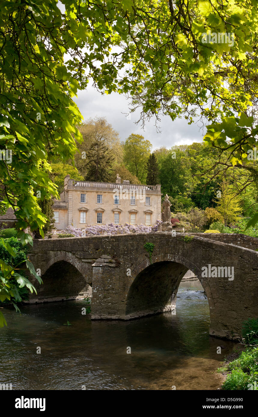 Georgian Manor House, entourée d'arbres dans un cadre rural à côté d'un pont en pierre et rivière. Banque D'Images