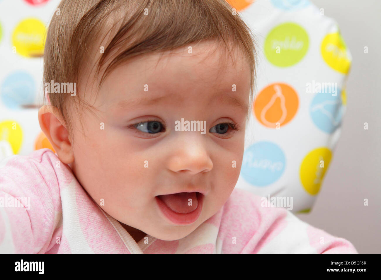 Huit mois baby girl wearing barboteuse rose représentée dans sa chaise haute sur sa première fête de Pâques. Banque D'Images