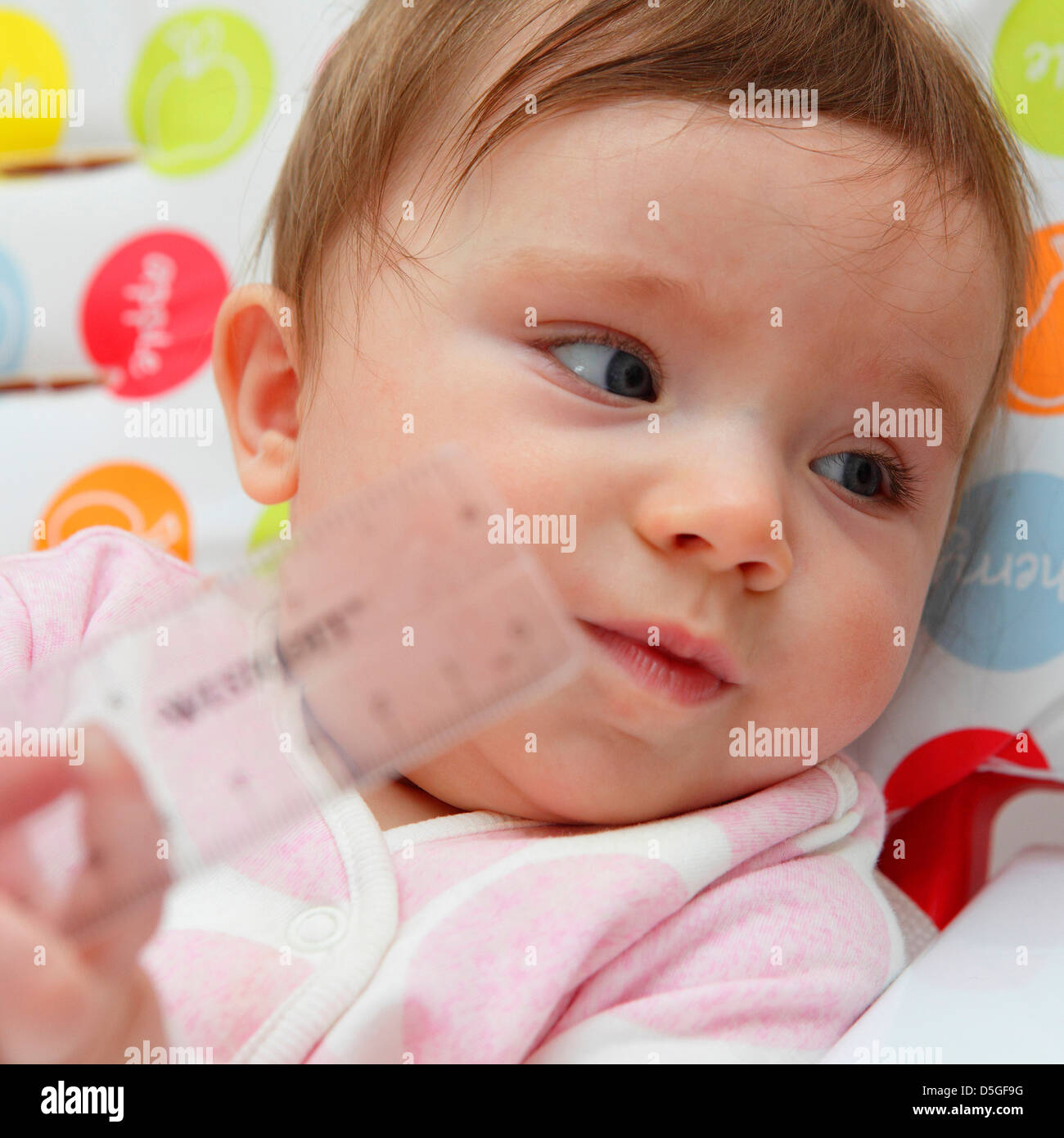 Huit mois baby girl wearing barboteuse rose représentée dans sa chaise haute sur sa première fête de Pâques. Banque D'Images