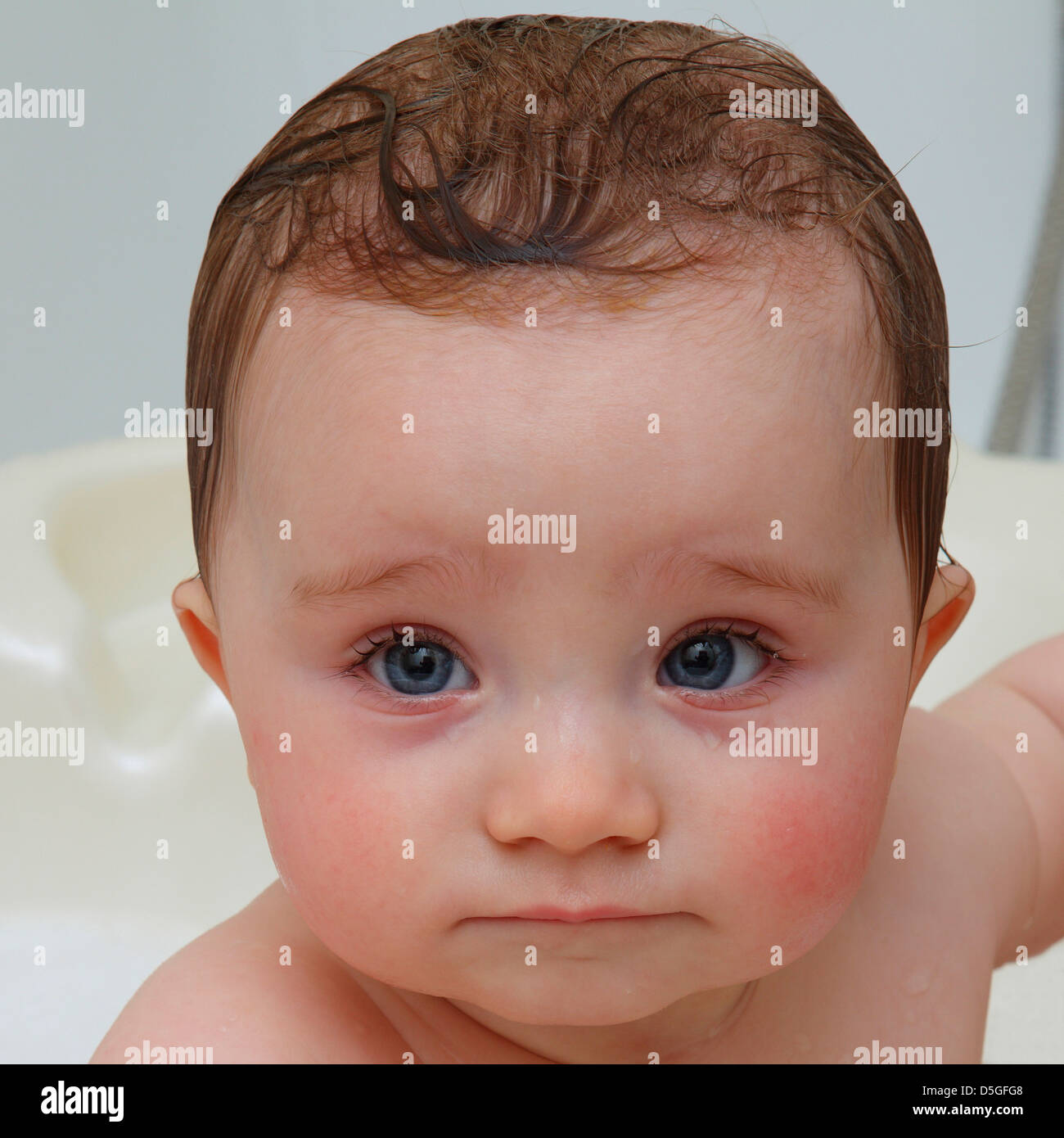Huit mois bébé fille à bath avec de grands yeux bleus et holding lèvre inférieure avec la lèvre supérieure et de grands yeux bleus. Banque D'Images