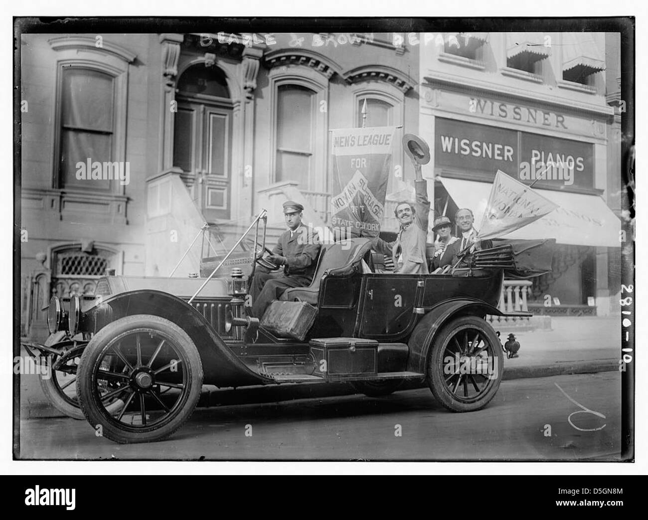 Une photographie montrant A.H. Brown et R.C. Beadle partant, avec un focus sur leur automobile. L’image comporte également une bannière liée au suffrage des femmes et à leur participation au mouvement. Banque D'Images