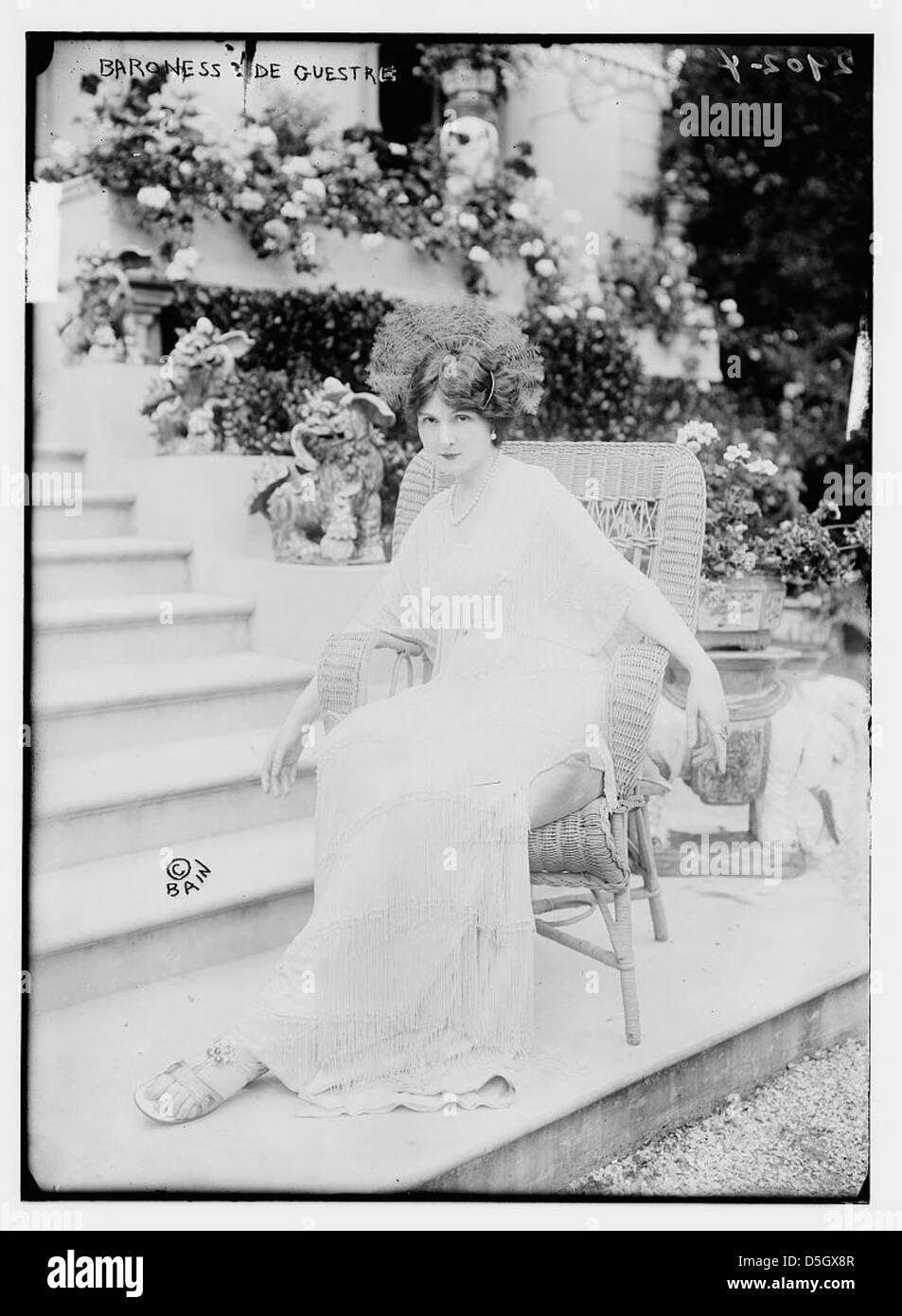 La baronne deGuestre est capturée assise à l'extérieur sur un escalier à Paris, en France. Elle est habillée avec élégance et entourée d'un jardin, reflétant le style de vie aristocratique de l'Europe du début du XXe siècle. Banque D'Images