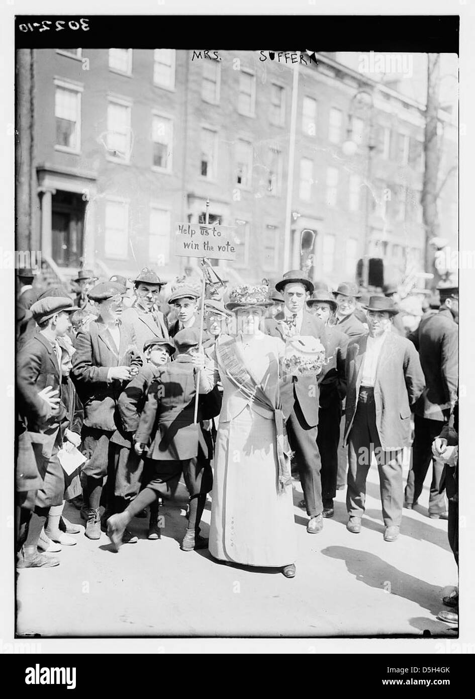 MRS Suffern, photographié le jour du suffrage à New York, tient à l'extérieur une pancarte en faveur du droit de vote des femmes. Elle porte une robe blanche et une écharpe, symbolisant sa participation au mouvement du suffrage. L'image la montre debout dans la rue aux côtés de garçons, reflétant la lutte en cours pour les droits des femmes et le mouvement pour le suffrage au début du XXe siècle. Banque D'Images