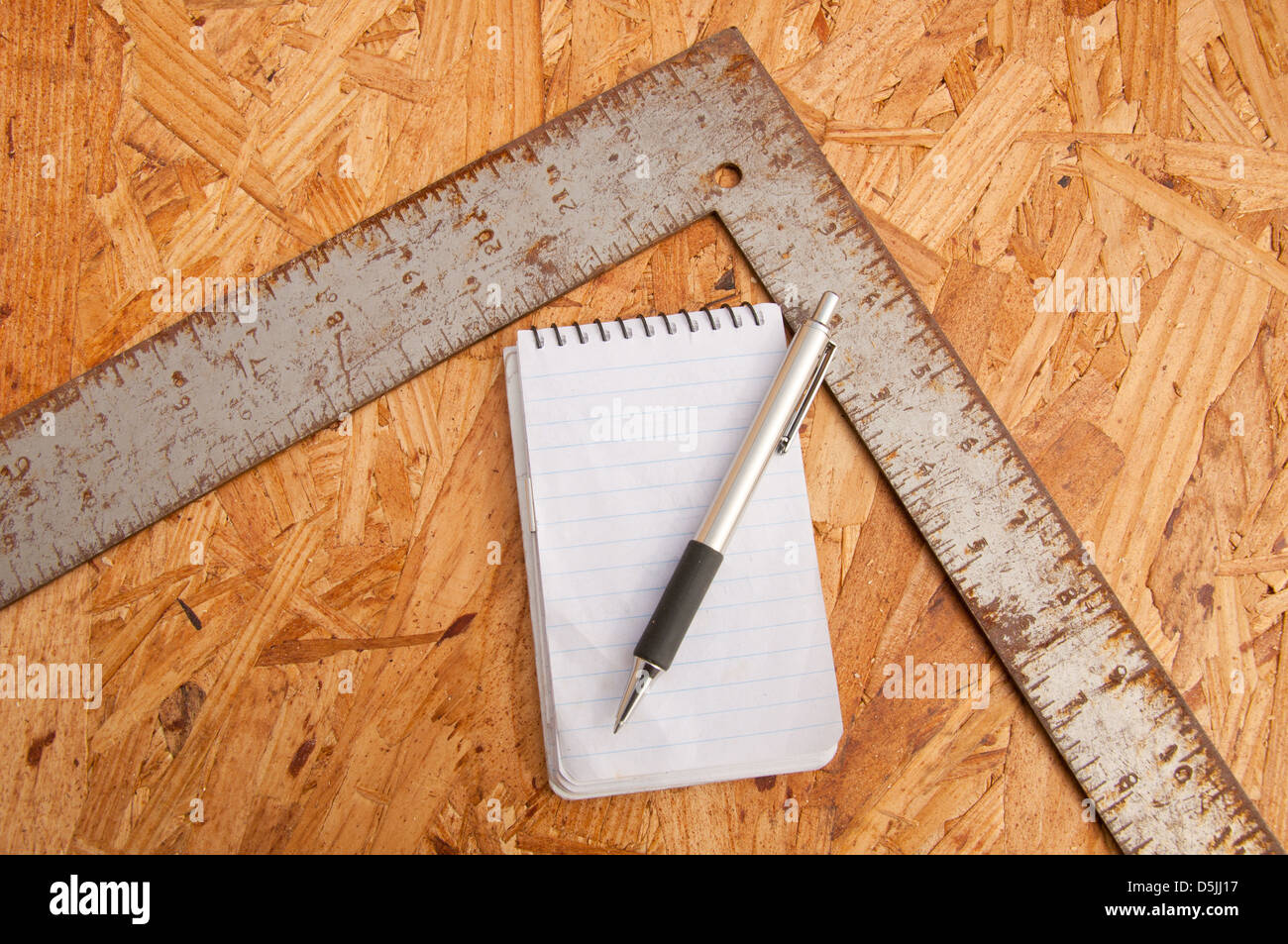 L'ossature du charpentier square, le bloc-notes et un stylo sur le dessus de copeaux agglomérés - concept de planification de travail du bois Banque D'Images