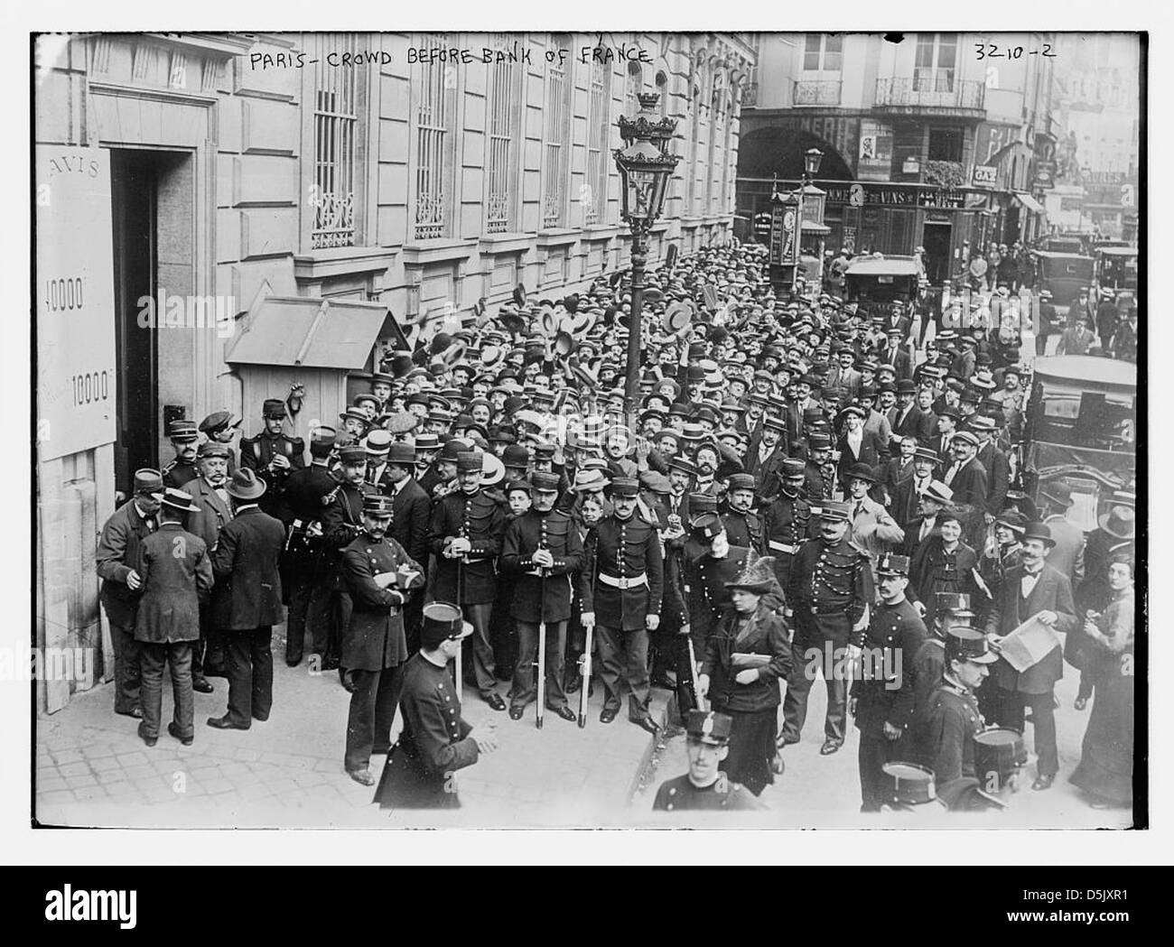 Cette photographie représente une foule réunie devant la Banque de France à Paris, capturant un moment historique du début du XXe siècle. L’image reflète l’atmosphère animée de la région et l’importance de la Banque de France dans l’économie du pays. Banque D'Images