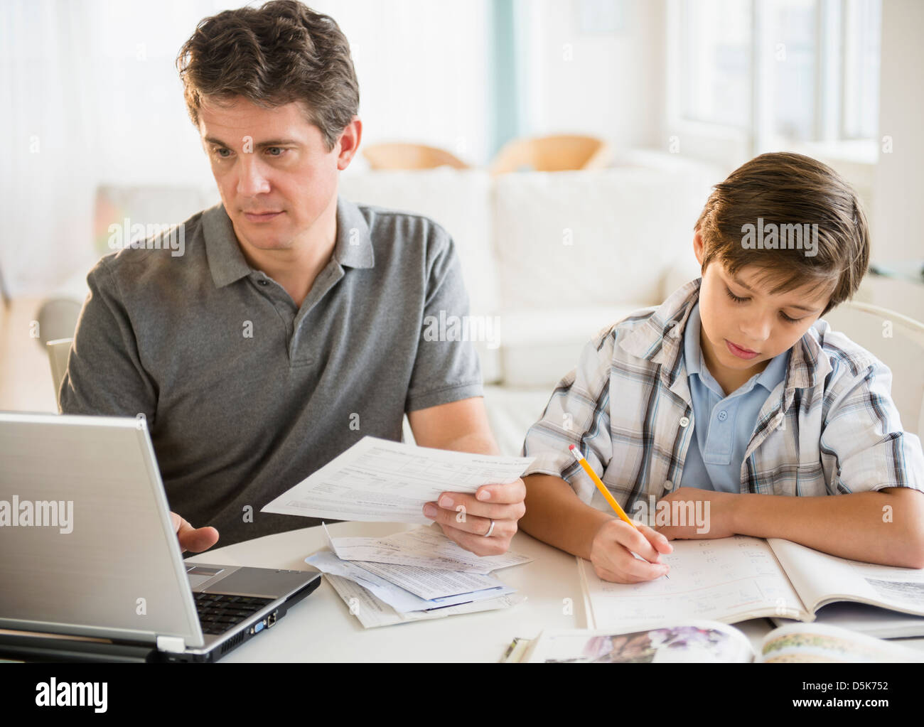 Père working on laptop and son (8-9) à faire leurs devoirs Banque D'Images