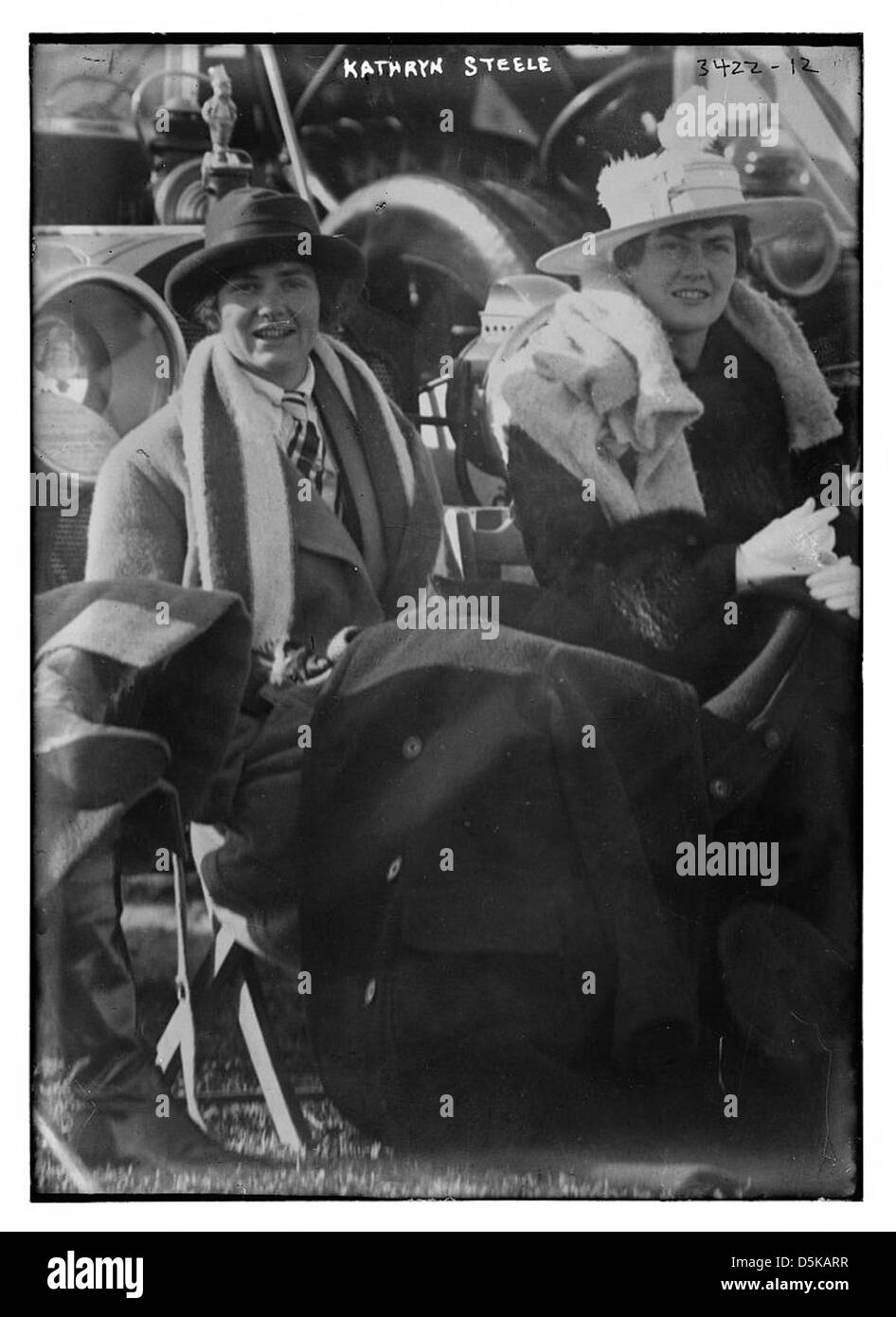 Kathryn Steele est capturée à l'extérieur sur long Island, portant un chapeau élégant et assise avec le sourire. L'image met en valeur sa mode dans un cadre décontracté et extérieur, probablement du début du XXe siècle. Banque D'Images