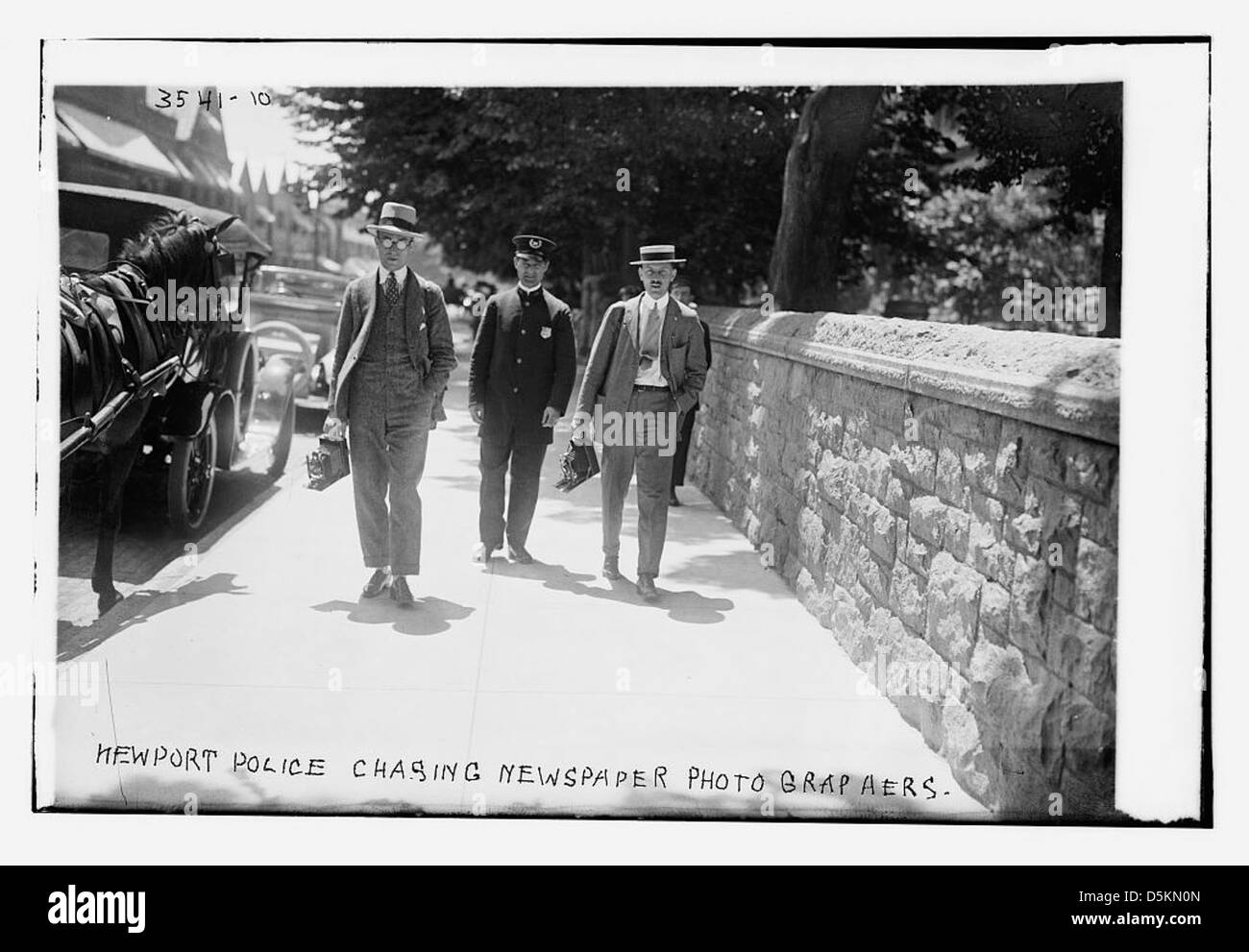Cette image représente des policiers de Newport poursuivant des photographes de journaux. Il capture un moment de tension entre les forces de l'ordre et la presse, mettant en lumière un conflit au début du XXe siècle. Banque D'Images