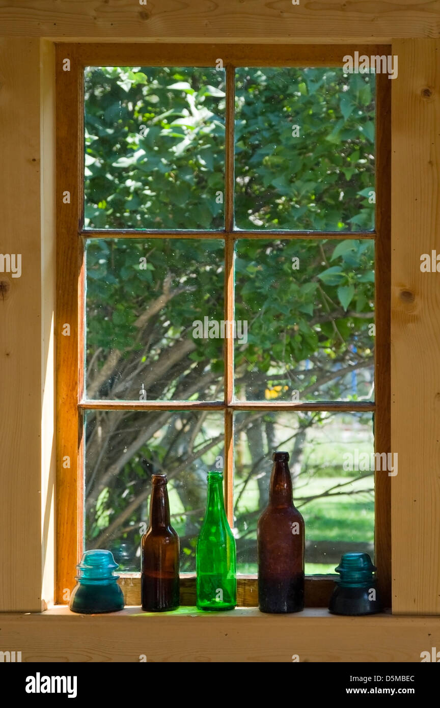 Une vieille ferme appui de fenêtre est titulaire de bouteilles et de verre ancien isolateurs télégraphiques qui capturent la lumière du matin. Banque D'Images