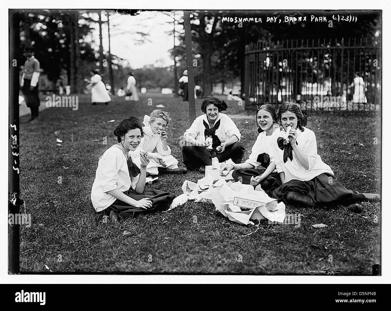 Cette photo en noir et blanc capture une scène de MidSummer Day au Bronx Park, New York, le 23 juin 1911. Il présente des jeunes femmes en costumes vintage, profitant d'un pique-nique dans le parc, capturant l'atmosphère joyeuse de l'été au début du XXe siècle. Banque D'Images