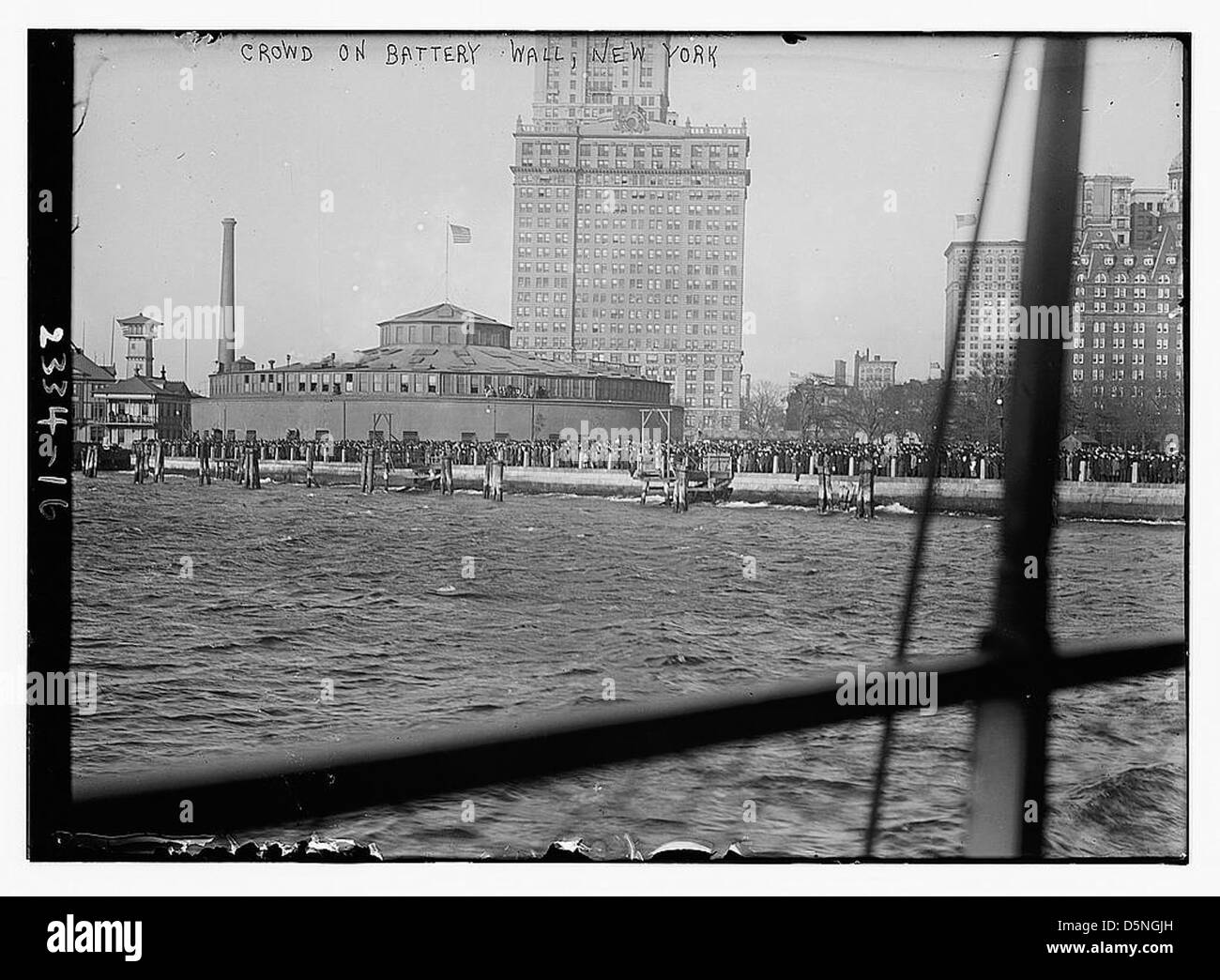 Cette photographie capture une foule rassemblée sur le Battery Wall à Lower Manhattan, New York, dans les années 1910 L'image offre un aperçu du port de New York, avec des bateaux et des monuments comme Castle Clinton visibles en arrière-plan. Banque D'Images