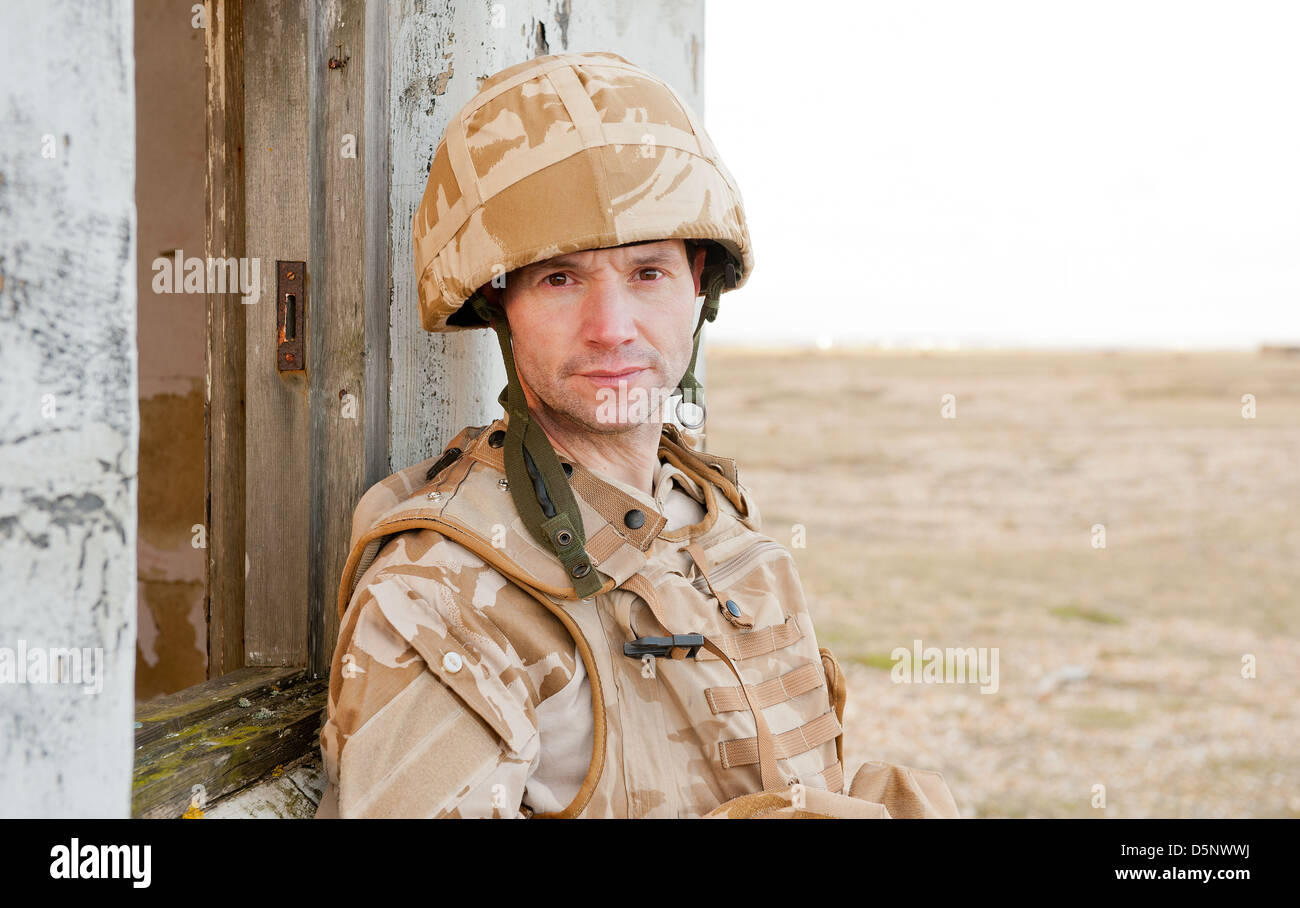British Soldier wearing camouflage de désert, regardant la caméra et appuyé contre un bâtiment abandonné. Banque D'Images
