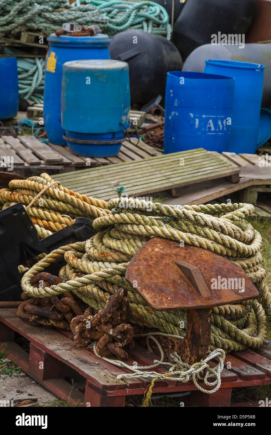 Corde enroulée, palettes en bois, Rusty anchor et baignoires en plastique sur le quai du port. Banque D'Images