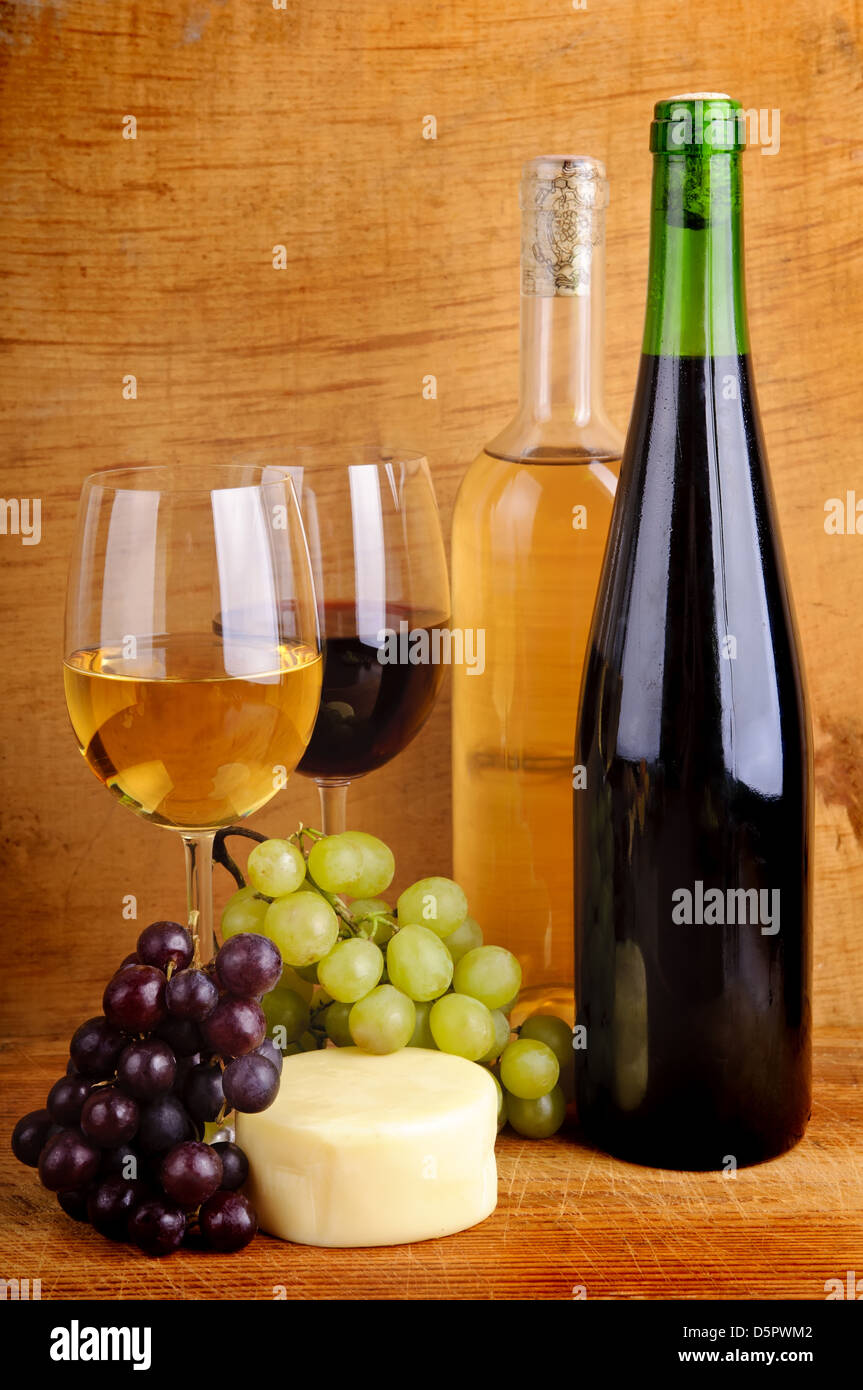 Nature morte avec du fromage, des raisins, du vin rouge et blanc en bouteilles et verres sur un fond de bois Banque D'Images