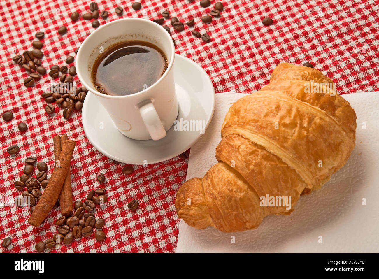 Tasse de café avec un croissant et des bâtons de cannelle et les grains de café sur la table. Banque D'Images