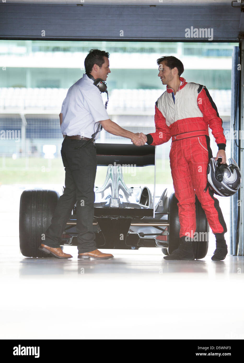 Racer et manager shaking hands in garage Banque D'Images