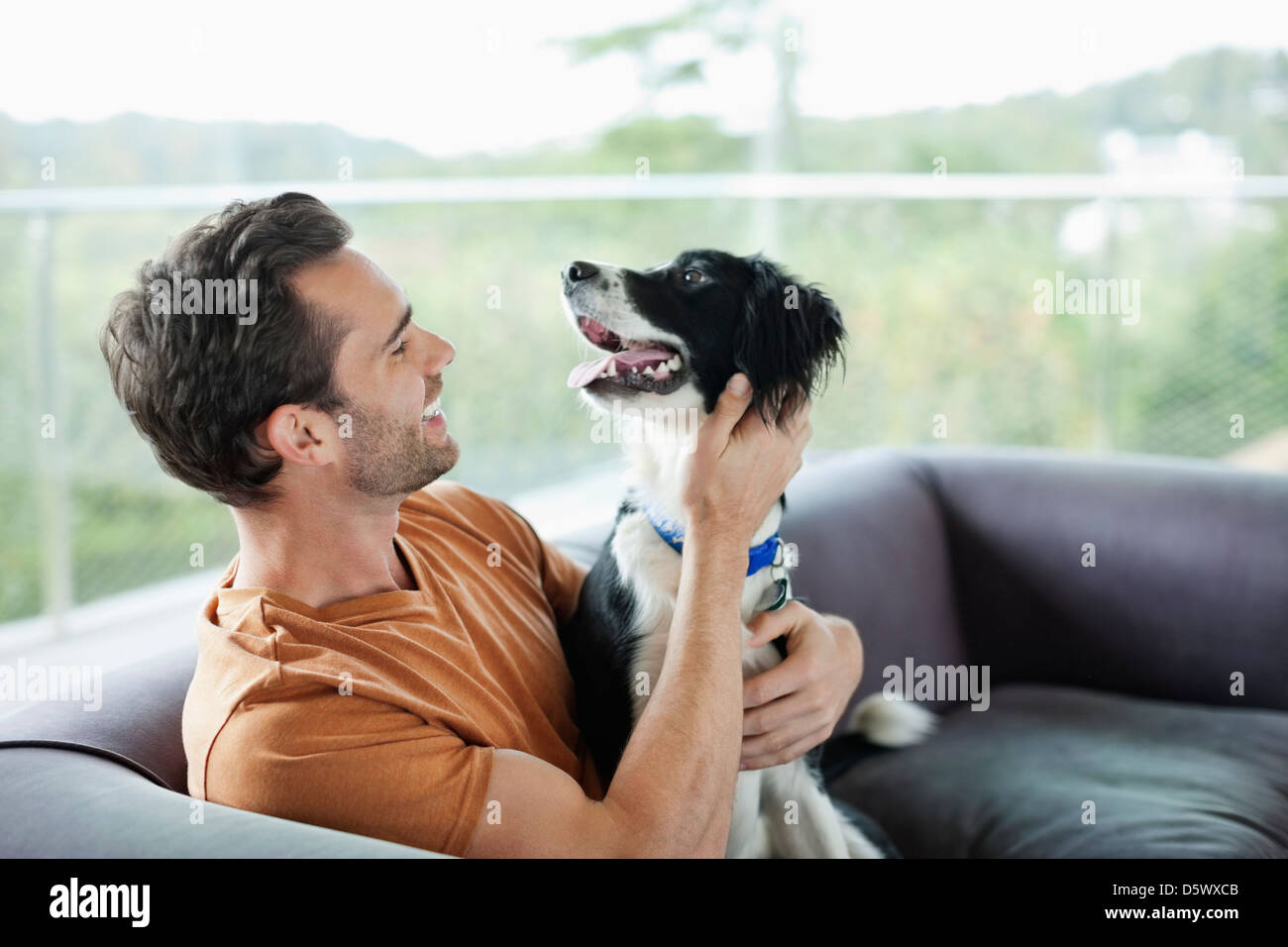 Smiling man petting dog on sofa Banque D'Images