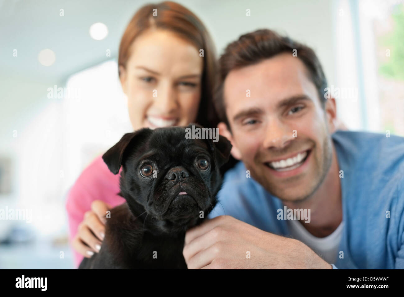 Smiling couple petting dog indoors Banque D'Images